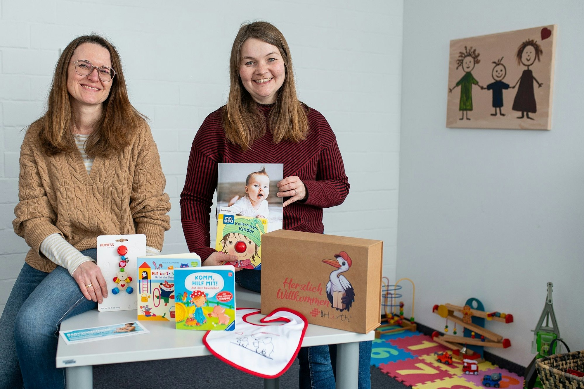 Auf dem Bild sind zwei Frauen mit Geschenken für Babys zu sehen