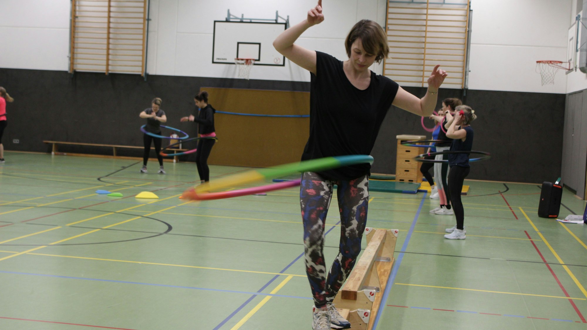 Eine Frau balanciert mit schwingendem Hula Hoop Reifen über einen schmalen Balken.