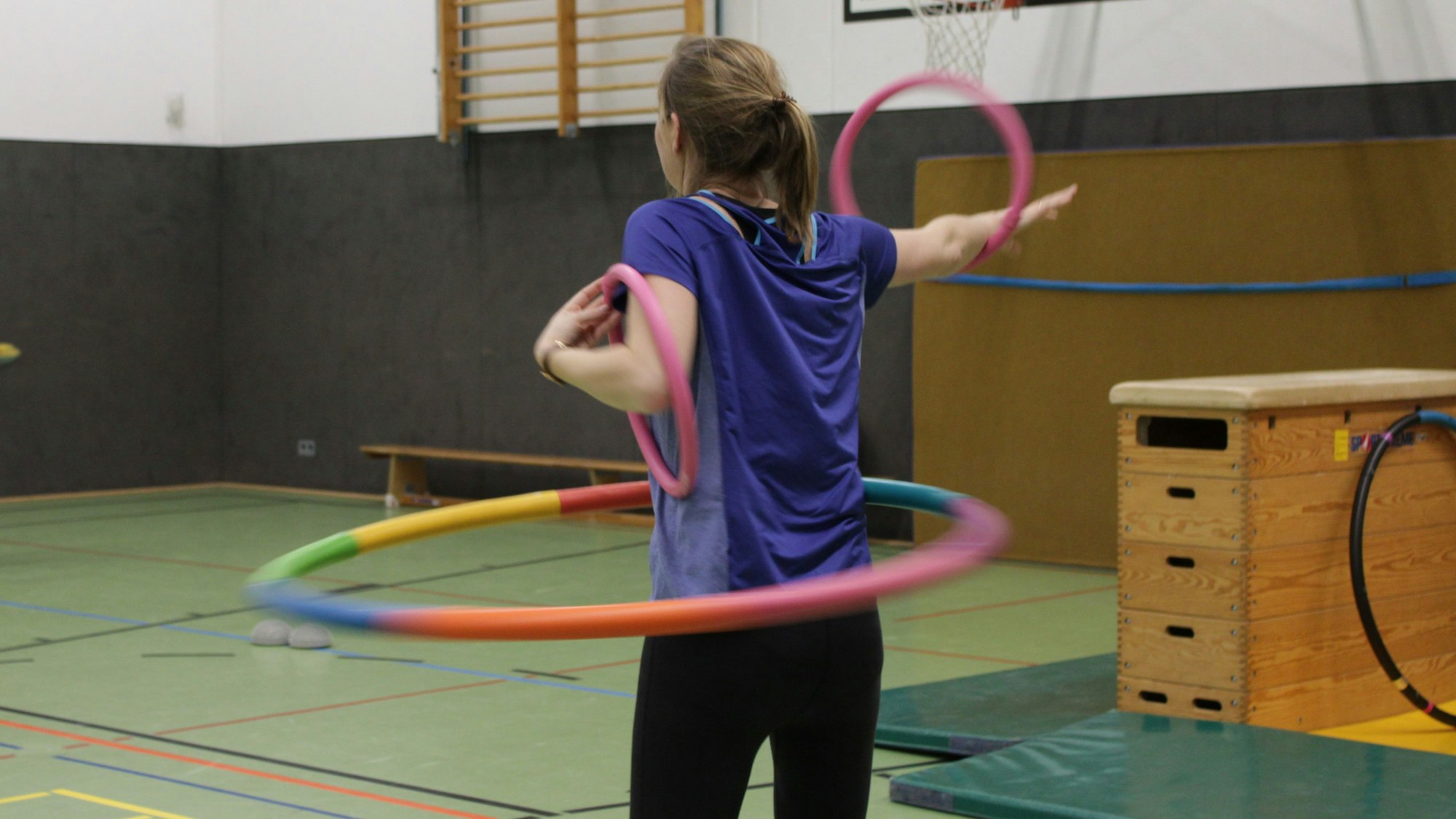 Eine Kursteilnehmerin kreist einen Reifen um die Hüfte und zwei kleinere Reifen um die Arme.