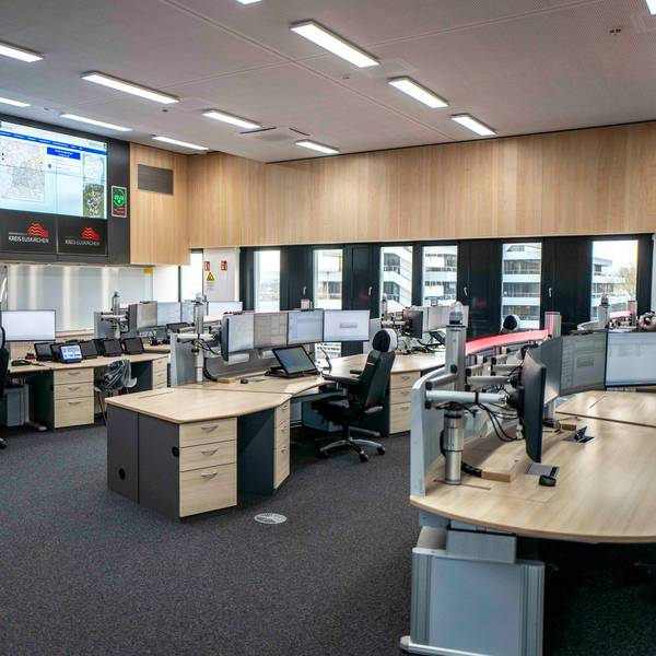Blick in den zentralen Raum der neuen Leitstelle in Euskirchen. Mehrere Disponenten-Pulte, jeweils ausgestattet mit vier Bildschirmen, sind zu sehen. Ausgerichtet sind die Arbeitsplätze auf riesige Bildschirme an der Wand, die bis zur Decke reichen.