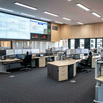 Blick in den zentralen Raum der neuen Leitstelle in Euskirchen. Mehrere Disponenten-Pulte, jeweils ausgestattet mit vier Bildschirmen, sind zu sehen. Ausgerichtet sind die Arbeitsplätze auf riesige Bildschirme an der Wand, die bis zur Decke reichen.