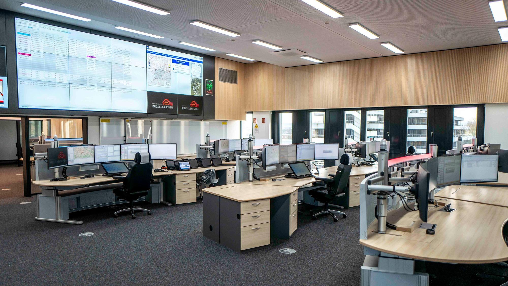 Blick in den zentralen Raum der neuen Leitstelle in Euskirchen. Mehrere Disponenten-Pulte, jeweils ausgestattet mit vier Bildschirmen, sind zu sehen. Ausgerichtet sind die Arbeitsplätze auf riesige Bildschirme an der Wand, die bis zur Decke reichen.