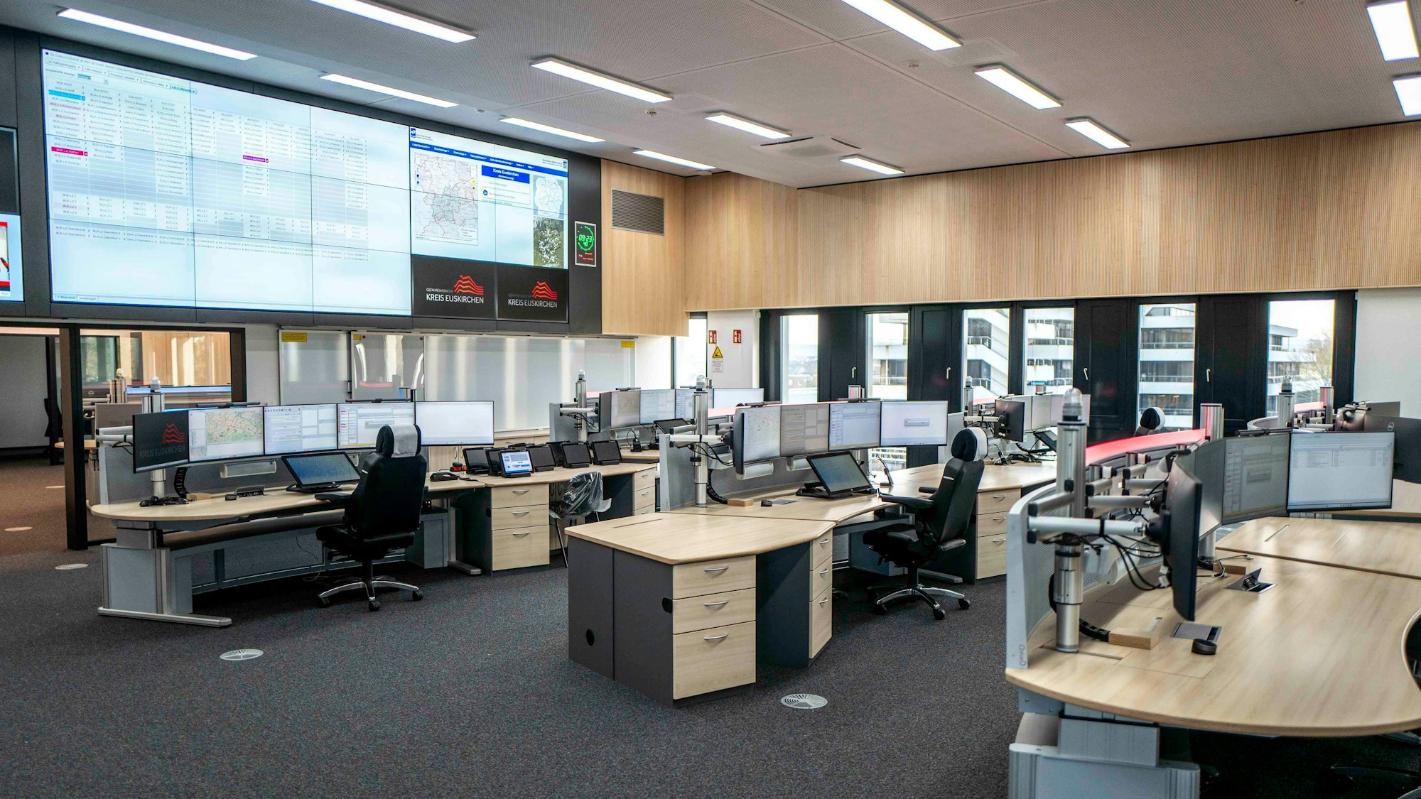 Blick in den zentralen Raum der neuen Leitstelle in Euskirchen. Mehrere Disponenten-Pulte, jeweils ausgestattet mit vier Bildschirmen, sind zu sehen. Ausgerichtet sind die Arbeitsplätze auf riesige Bildschirme an der Wand, die bis zur Decke reichen.
