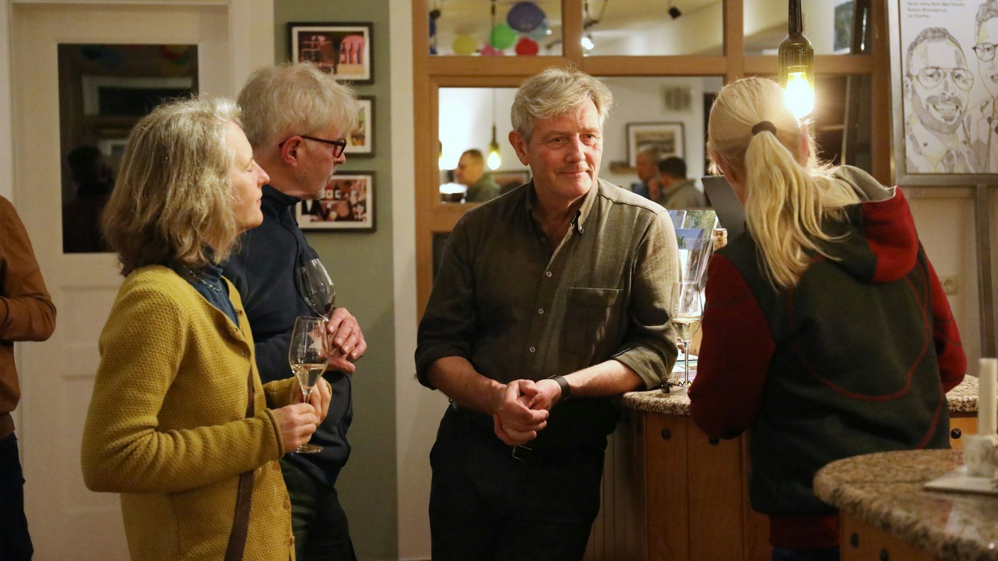 Vier Winzer stehen zusammen und unterhalten sich, zwei Frauen und zwei Männer. In der Hand halten sie Gläser mit Weißwein.