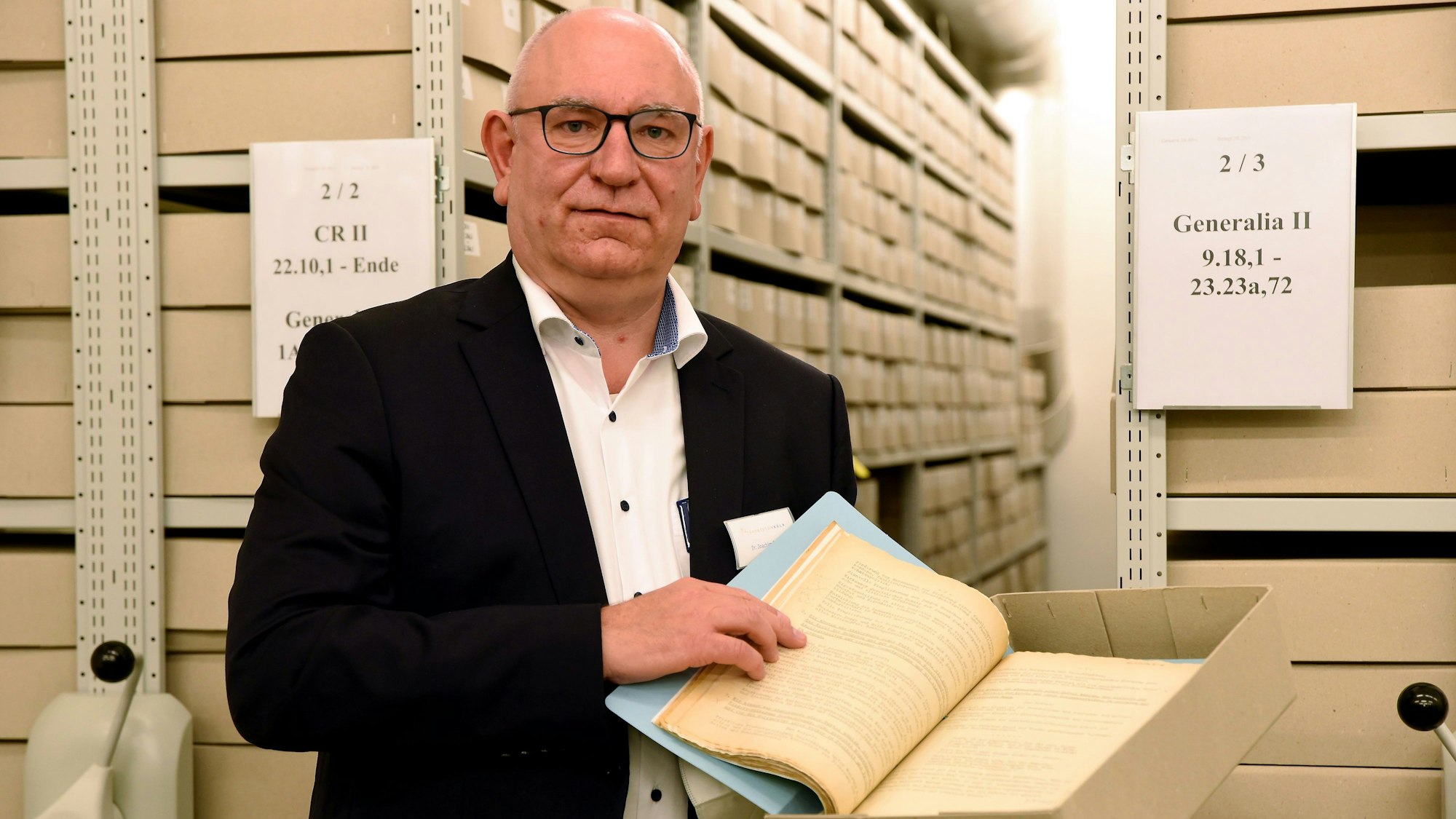 Joachim Oepen steht im Archiv vor einer Regalwand, er hat einen Karton mit einer alten Schrift in der Hand.