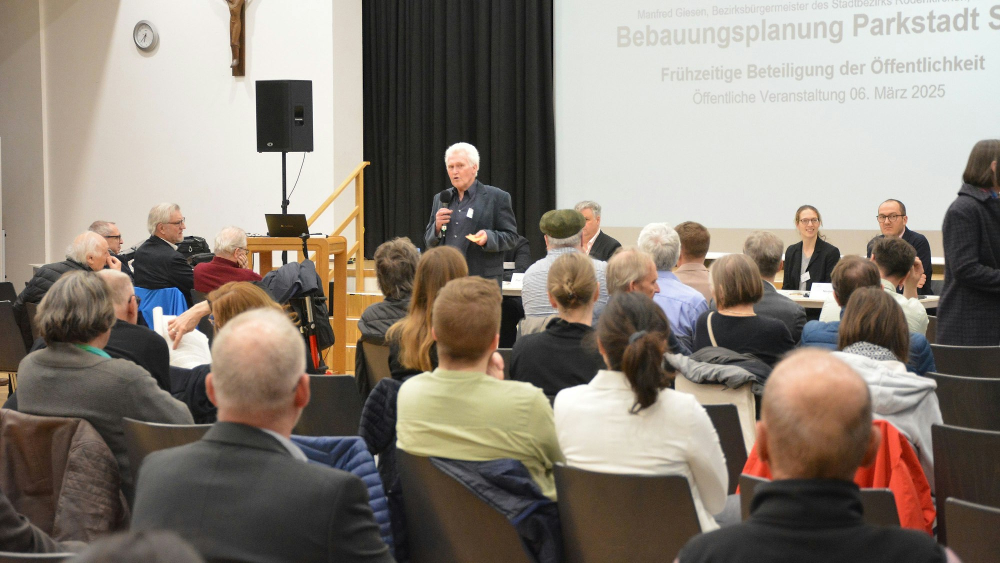 Ein Mann mit Mikrofon steht vor Menschen und spricht.