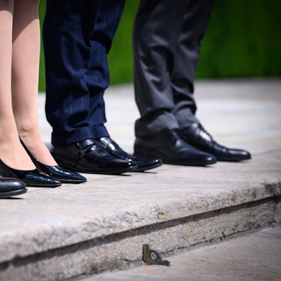 Eine Frau steht zwischen drei Männern in Anzügen auf Treppenstufen.