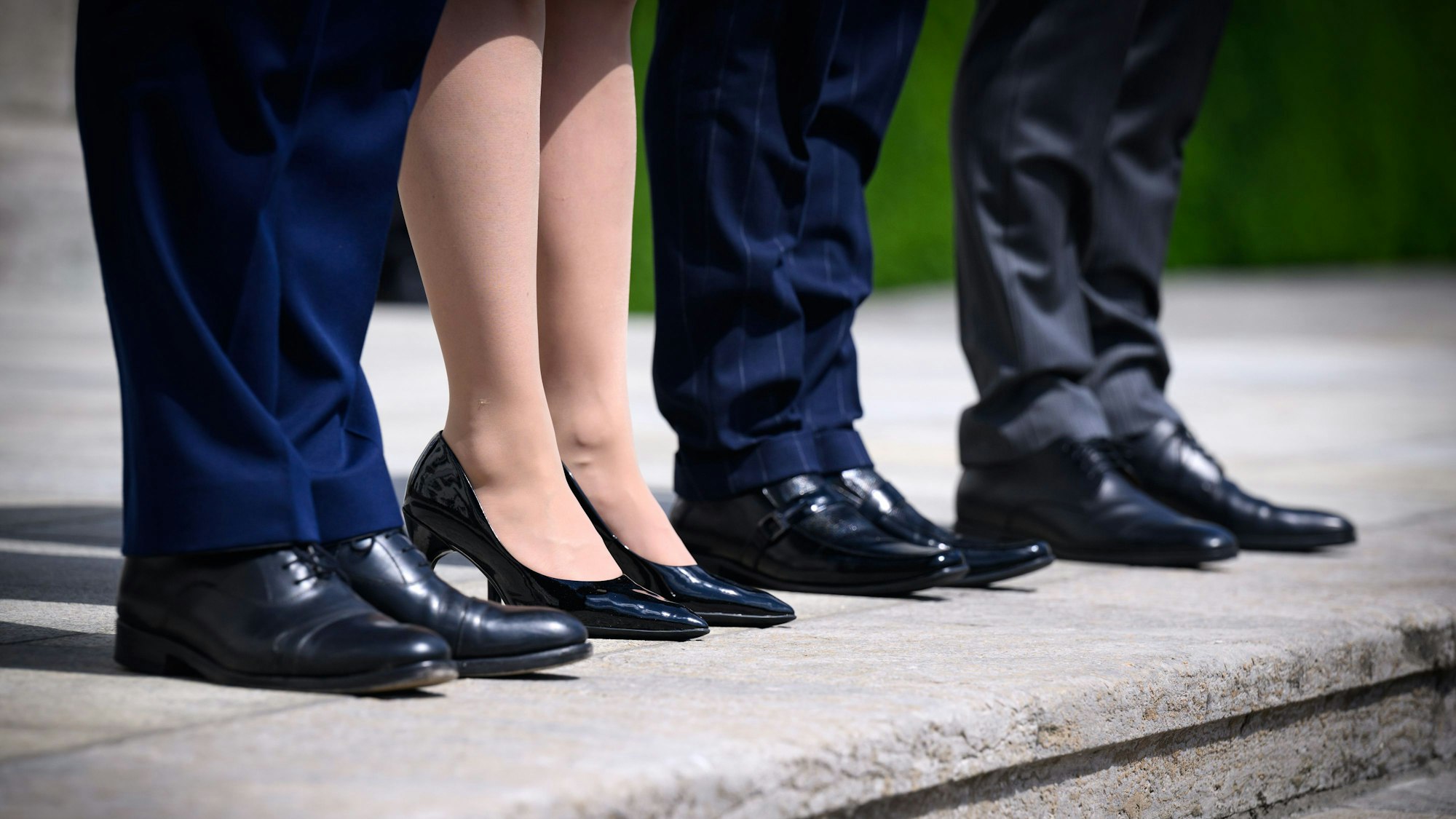 Eine Frau steht zwischen drei Männern in Anzügen auf Treppenstufen.