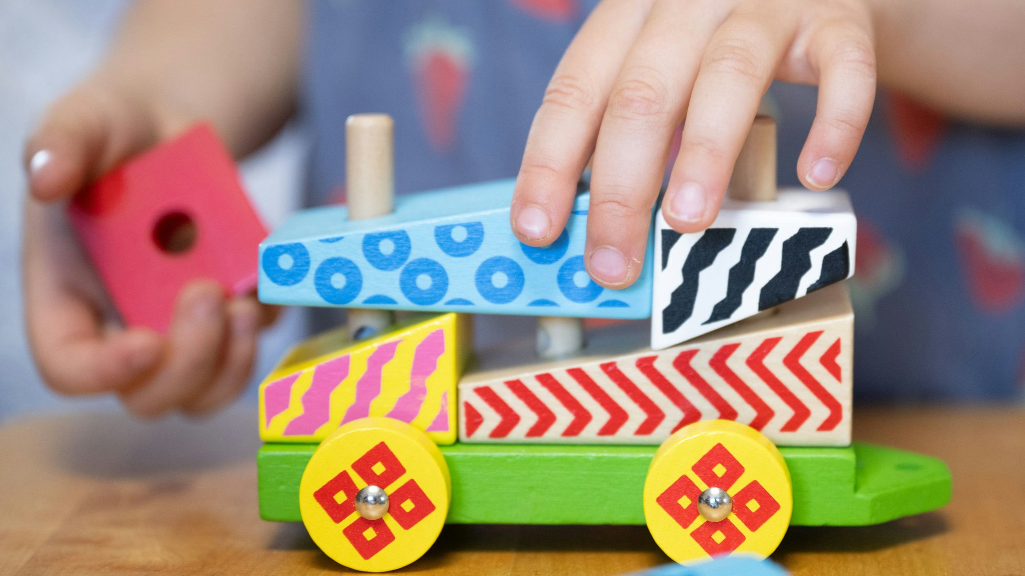 Man sieht eine Kinderhand, die ein Auto aus Holzbausteinen schiebt.