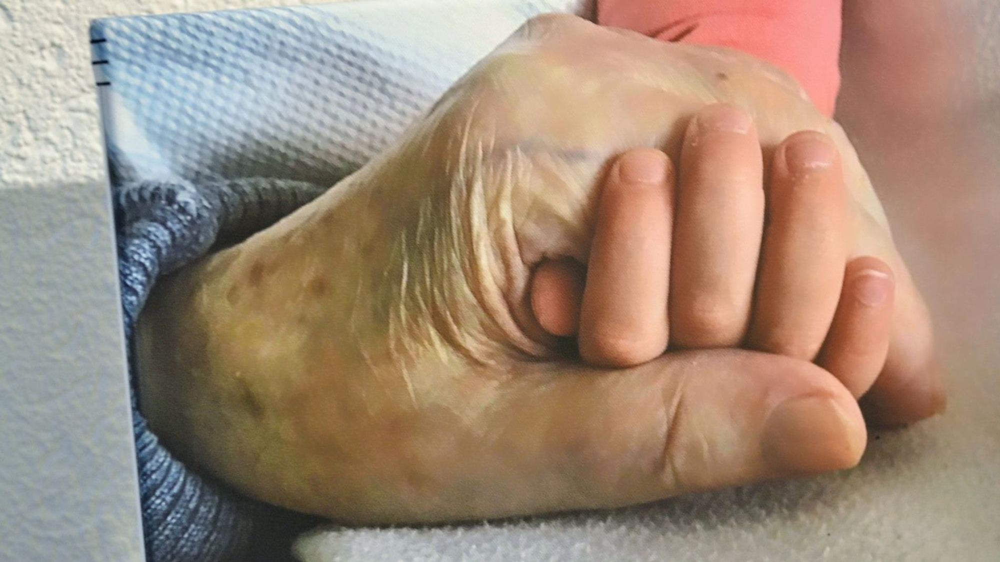 Auf einem Bild sind die Hand eines alten Menschen und die Hand eines kleinen Kindes zu sehen.