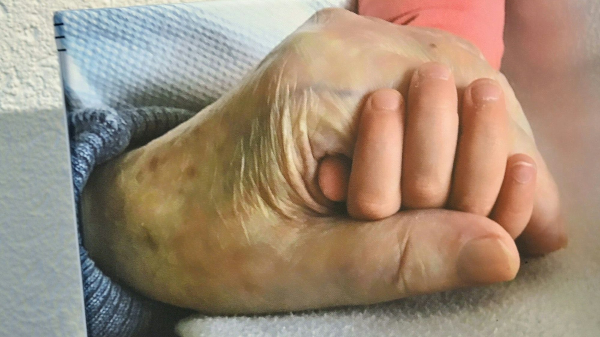 Auf einem Bild sind die Hand eines alten Menschen und die Hand eines kleinen Kindes zu sehen.