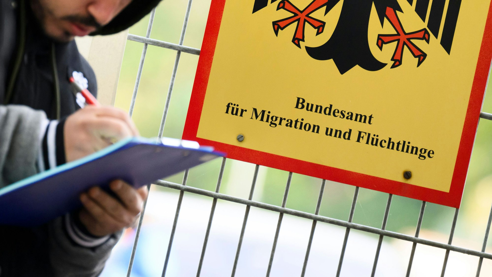 Ein Mann füllt ein Formular aus neben einem Schild vom Bundesamt für Migration und Flüchtlinge an der Landesaufnahmebehörde Niedersachsen am Standort Braunschweig.