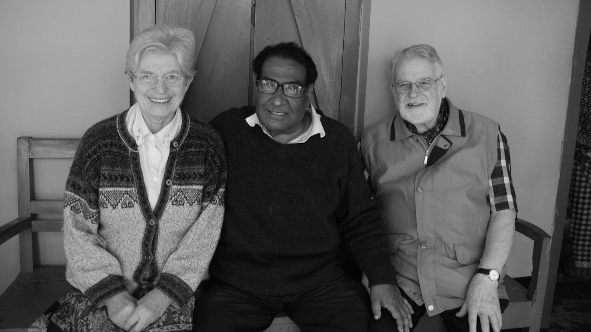 Eine Frau und zwei Männer sitzen auf einer Bank.