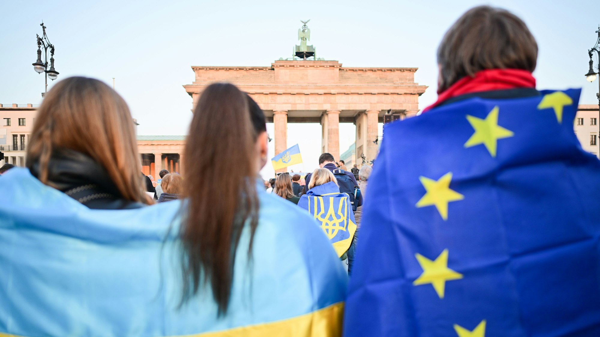 Teilnehmer stehen mit Ukraine- und EU-Fahnen während einer Demonstration für Solidarität mit der Ukraine „Stand with Ukraine“ vor dem Brandenburger Tor.