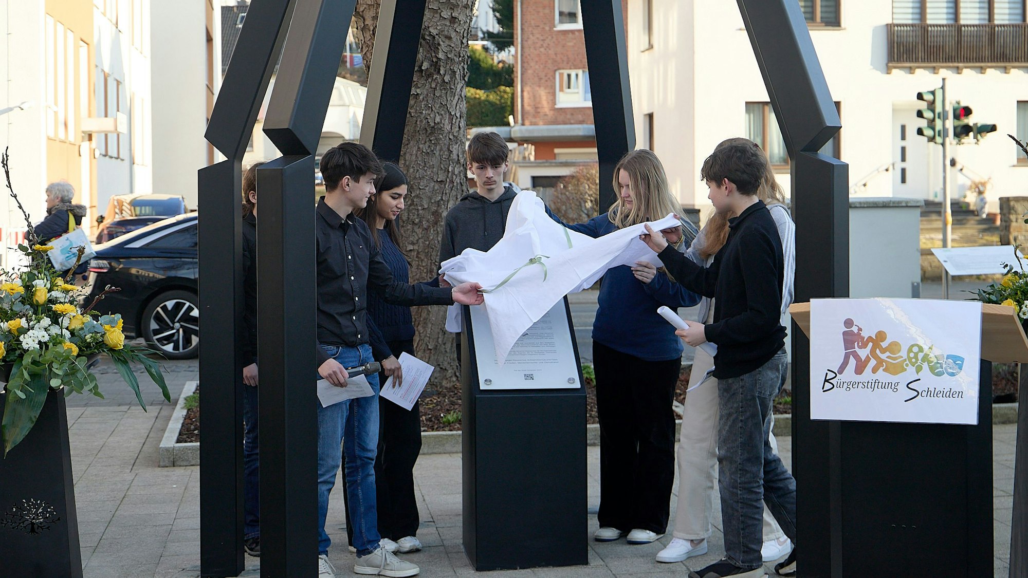 Eine Gruppe Jugendliche zieht ein Tuch von einer Gedenktafel.