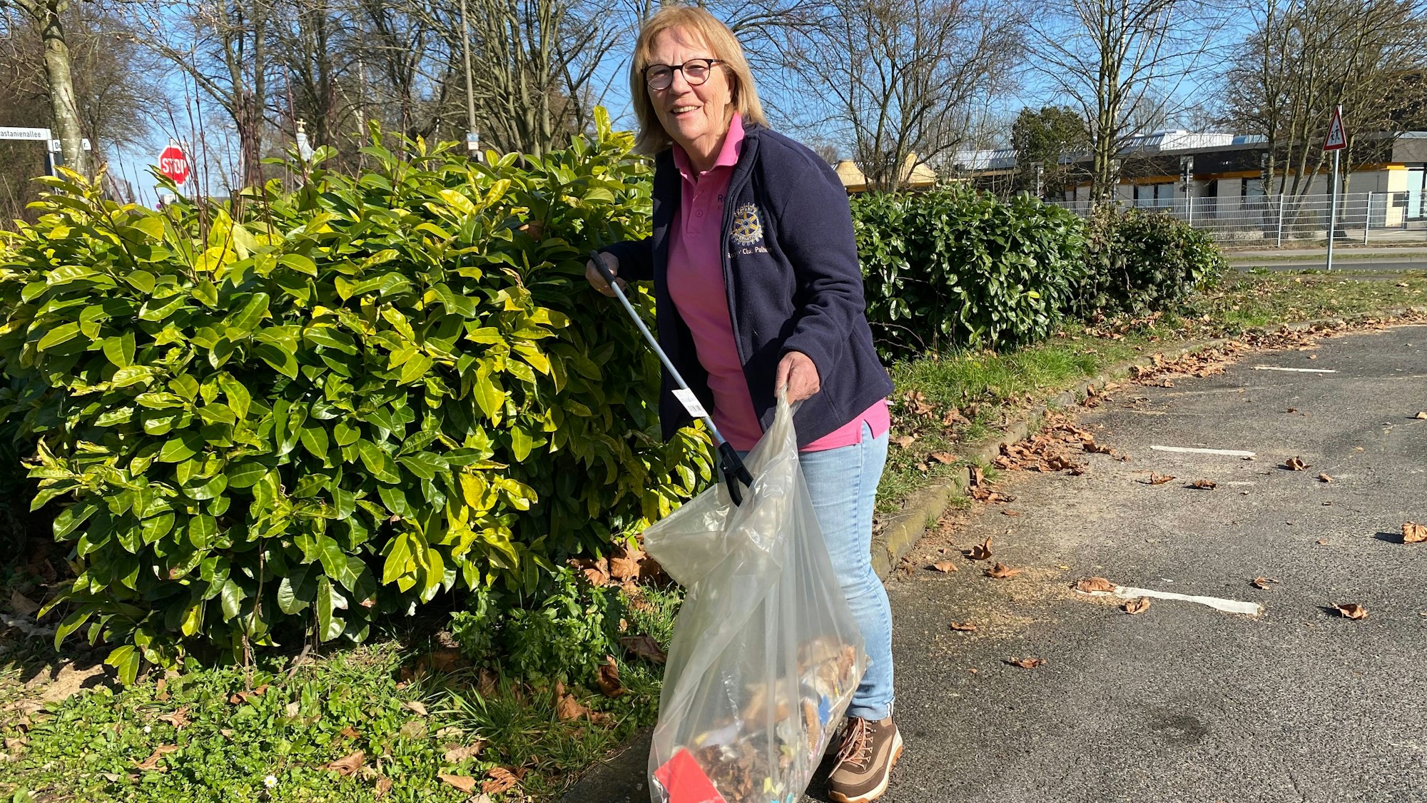 Ein Frau sammelt Müll. Sie hält eine riesige Plastiktüte in der einen und einen Greifzange in der anderen Hand.