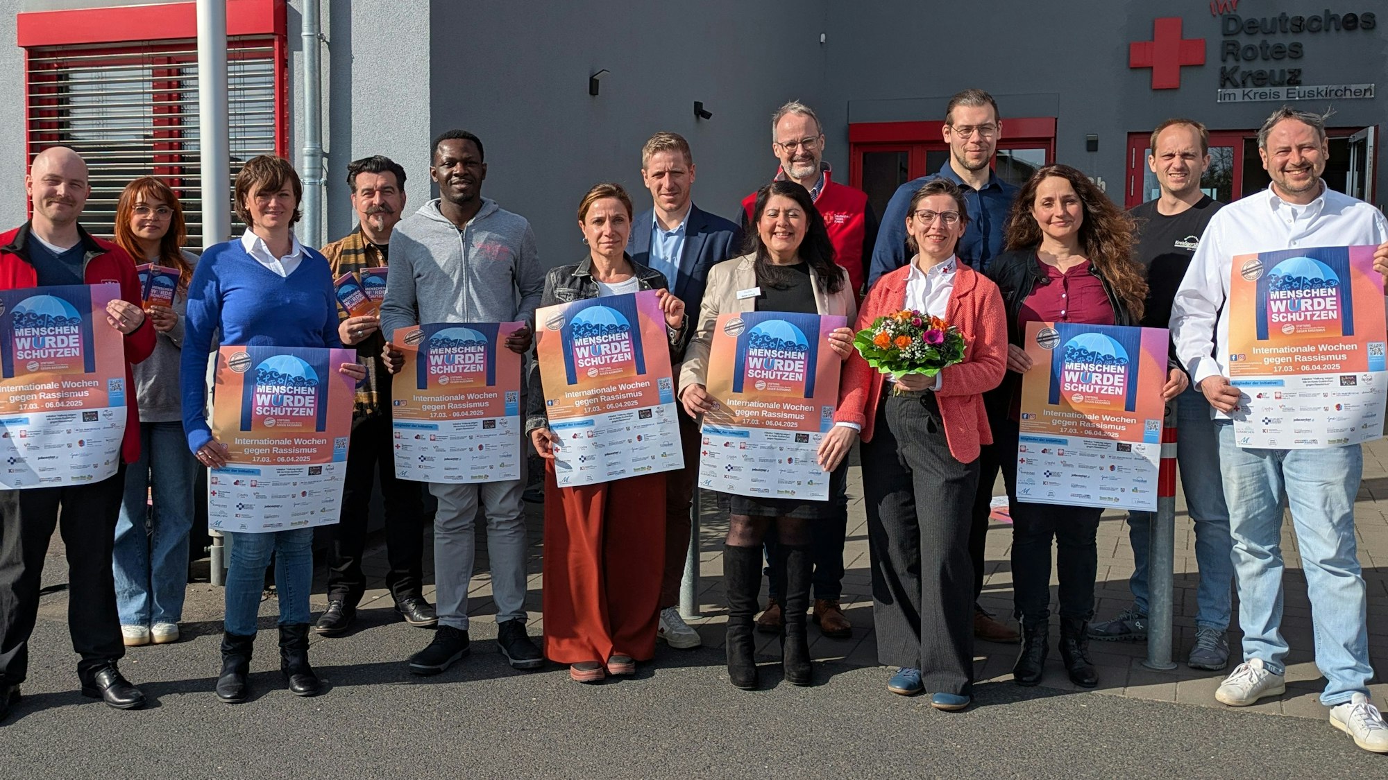 Eine Gruppe Menschen steht vor einem Gebäude des Deutschen Roten Kreuzes und hält Plakate in die Kamera.