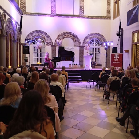 Auf der Bühne steht ein Konzertflügel, violette Ballons sorgen für festliche Stimmung.