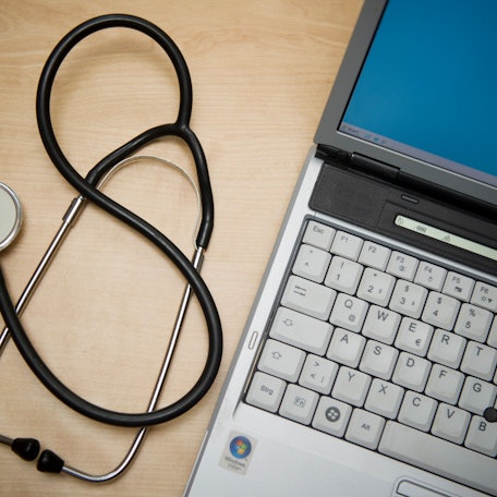 Ein Stethoskop liegt neben einem Laptop.