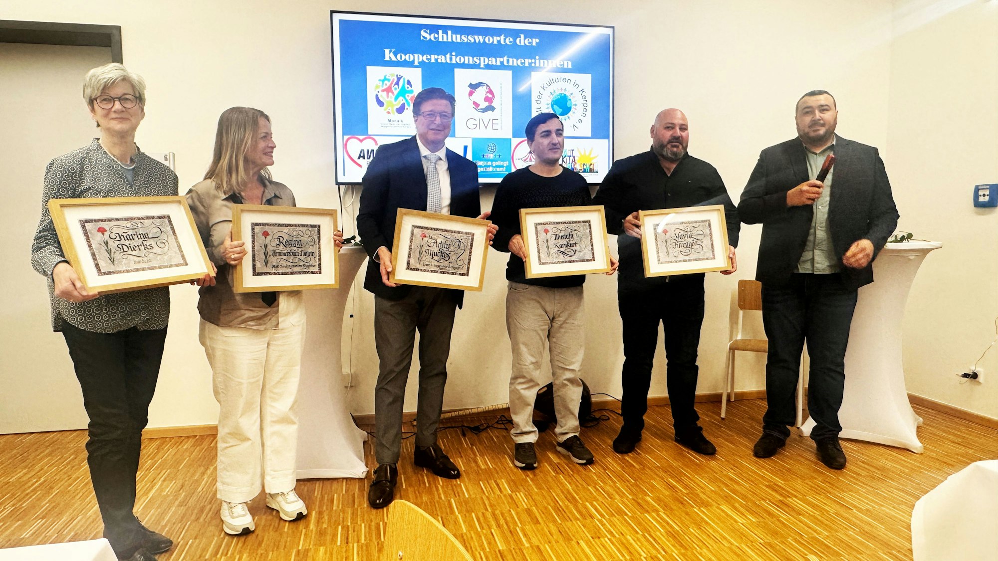 Auf dem Bild stehen Karina Dierks, Regina Hemmersbach-Fontein, Addy Muckes, Mustafa Karakurt, Yavuz Karagöz in einer Reihe und halten Kalligrafien ihres Namens hoch. Daneben steht der Laudator Murat Gök.