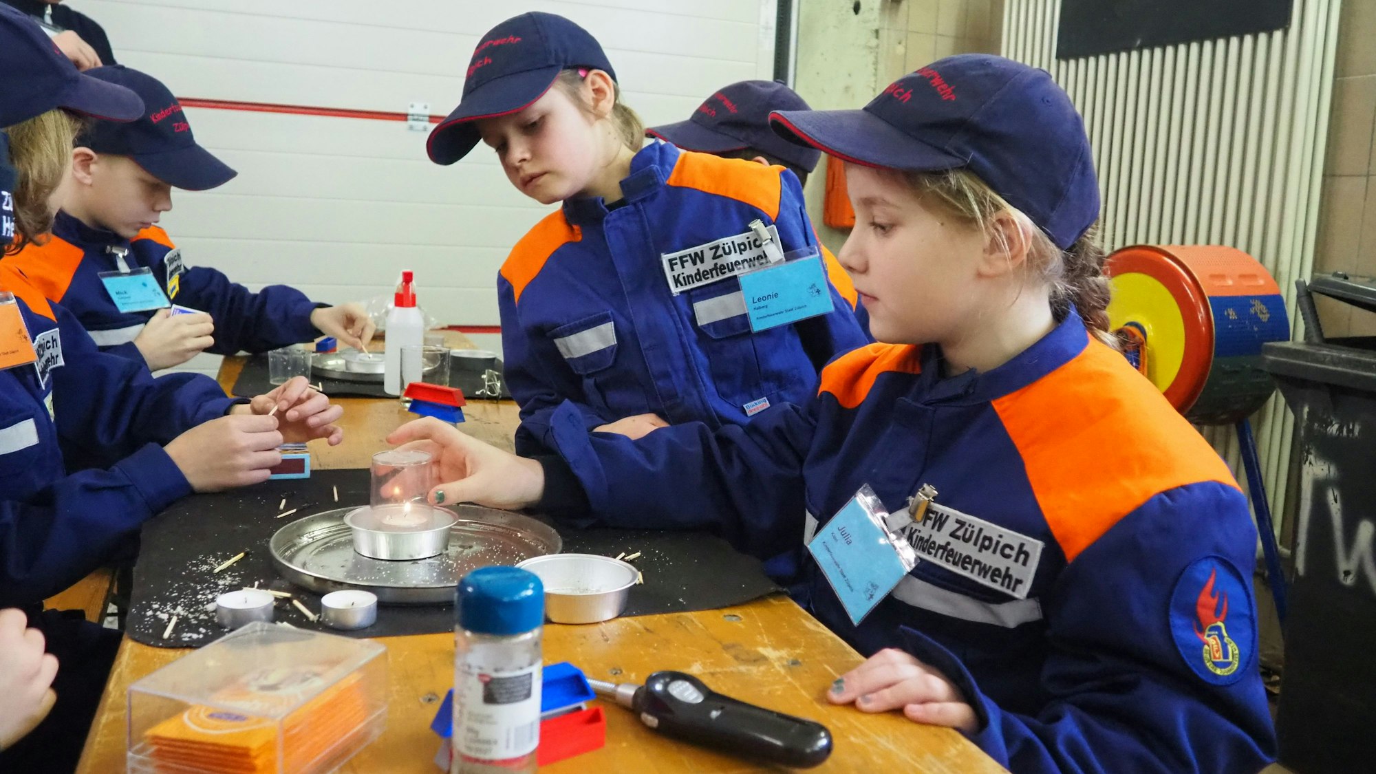 Kinder in orange-blauen Jacken sitzen an einem Tisch und experimentieren.