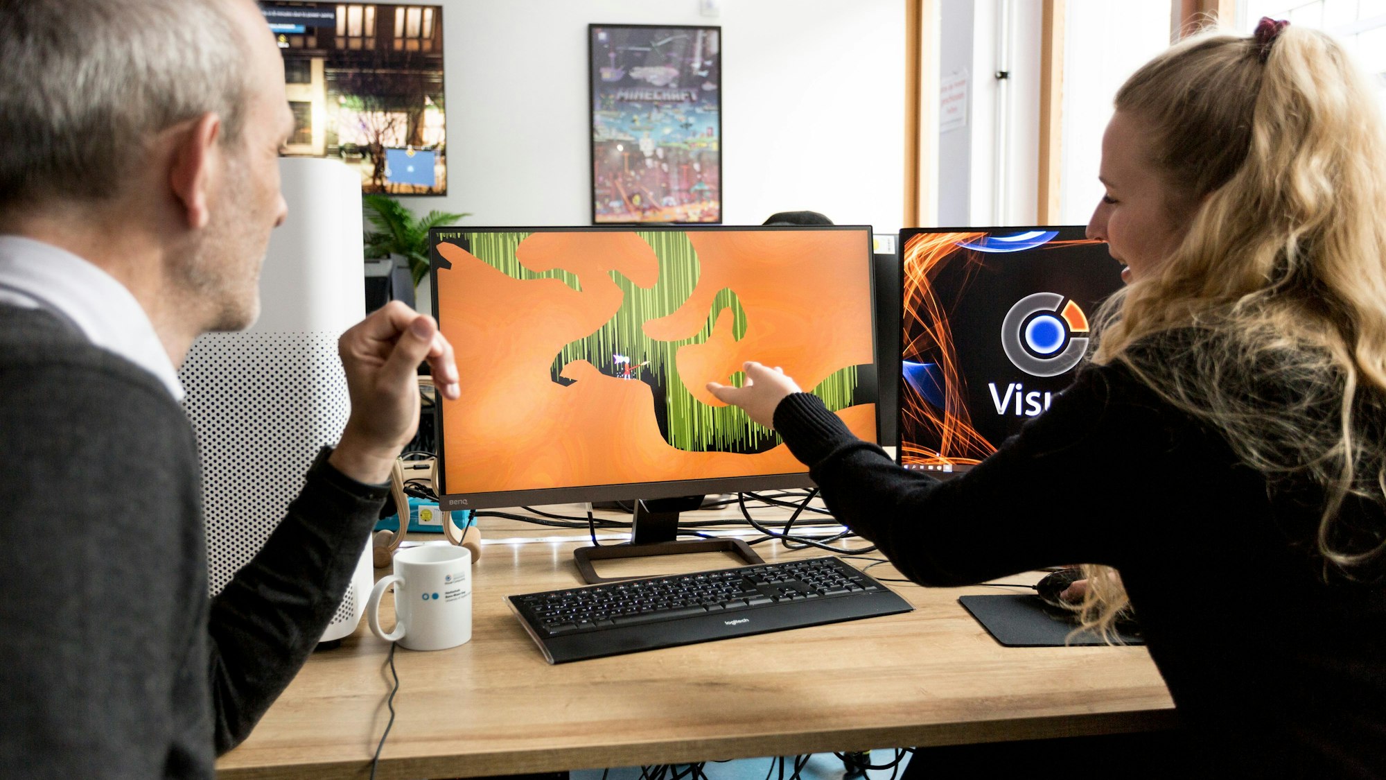 Eine junge Frau und ein älterer Mann sitzen am Schreibtisch vor einem Computerbildschirm.