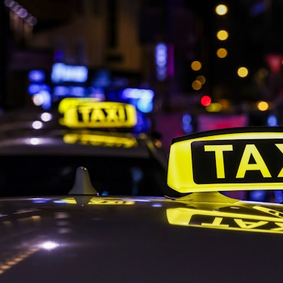 Ein Taxi mit beleuchtetem Taxischild wartet in einer Schlange von Taxen auf Fahrgäste.