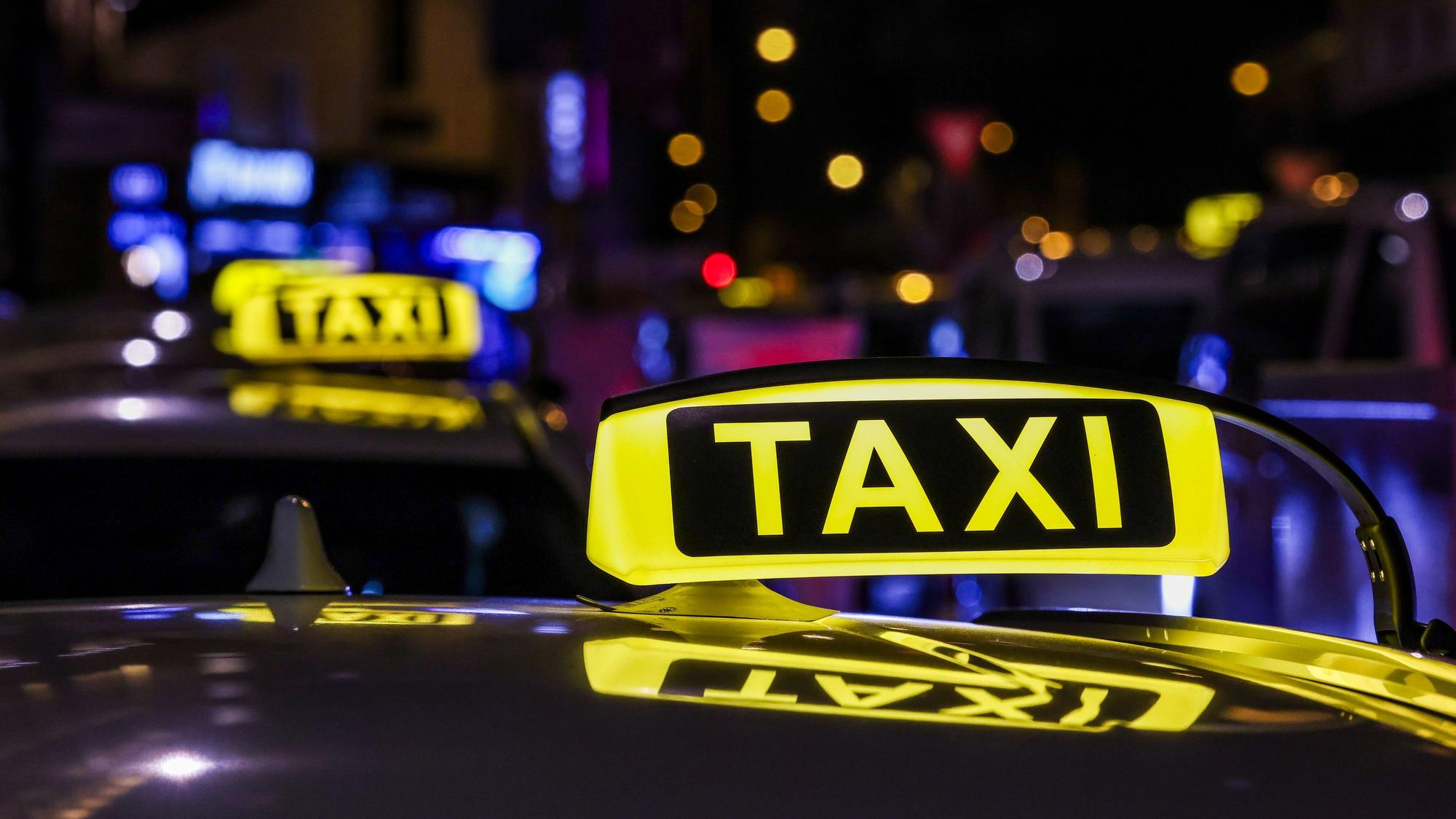 Ein Taxi mit beleuchtetem Taxischild wartet in einer Schlange von Taxen auf Fahrgäste.