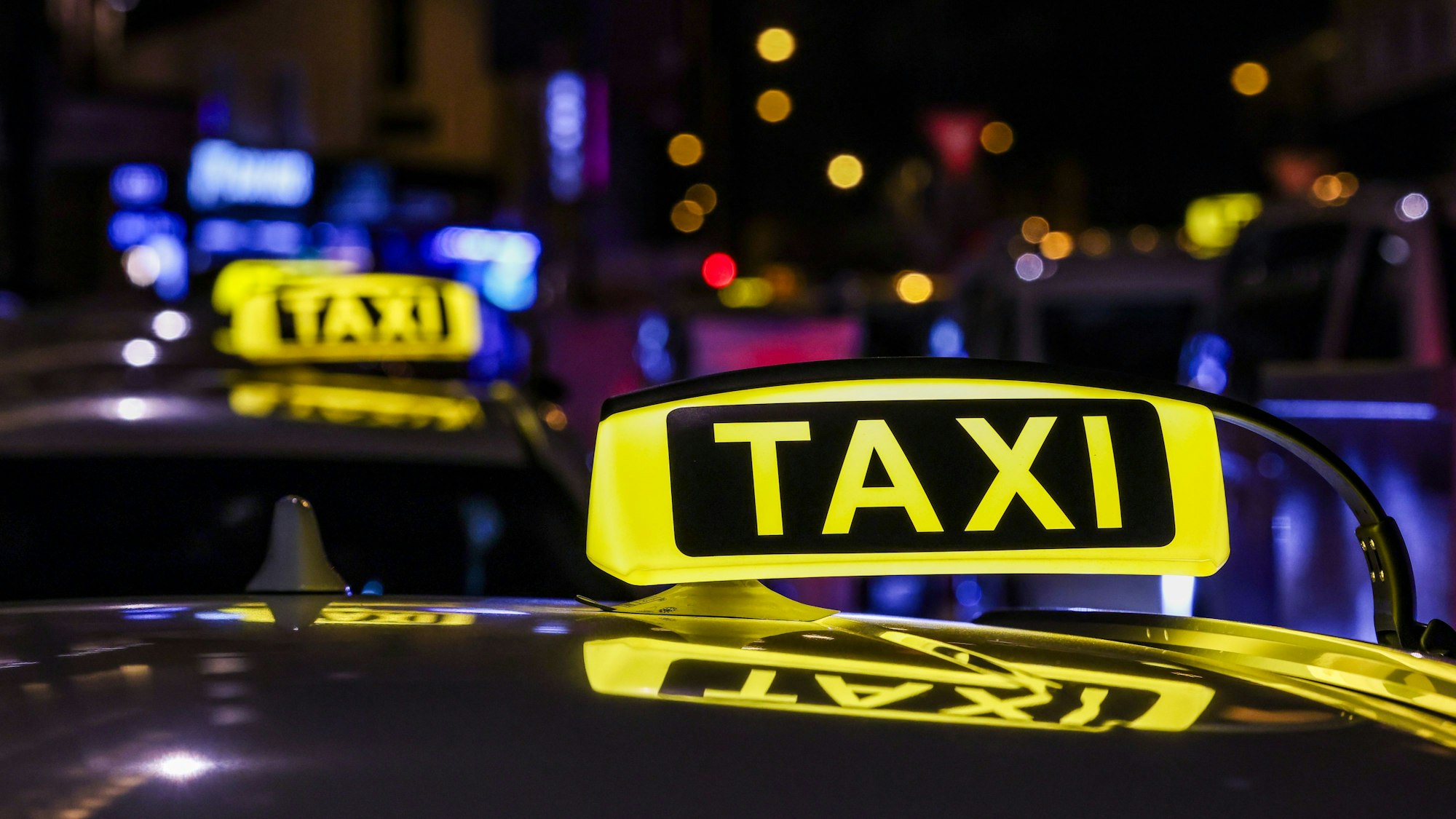 Ein Taxi mit beleuchtetem Taxischild wartet in einer Schlange von Taxen auf Fahrgäste.