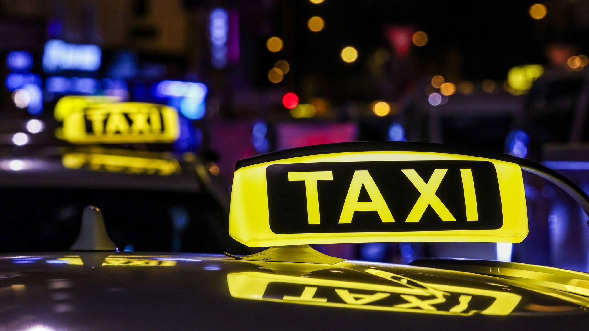 Ein beleuchtetes Taxischild auf dem Dach eines Taxis.