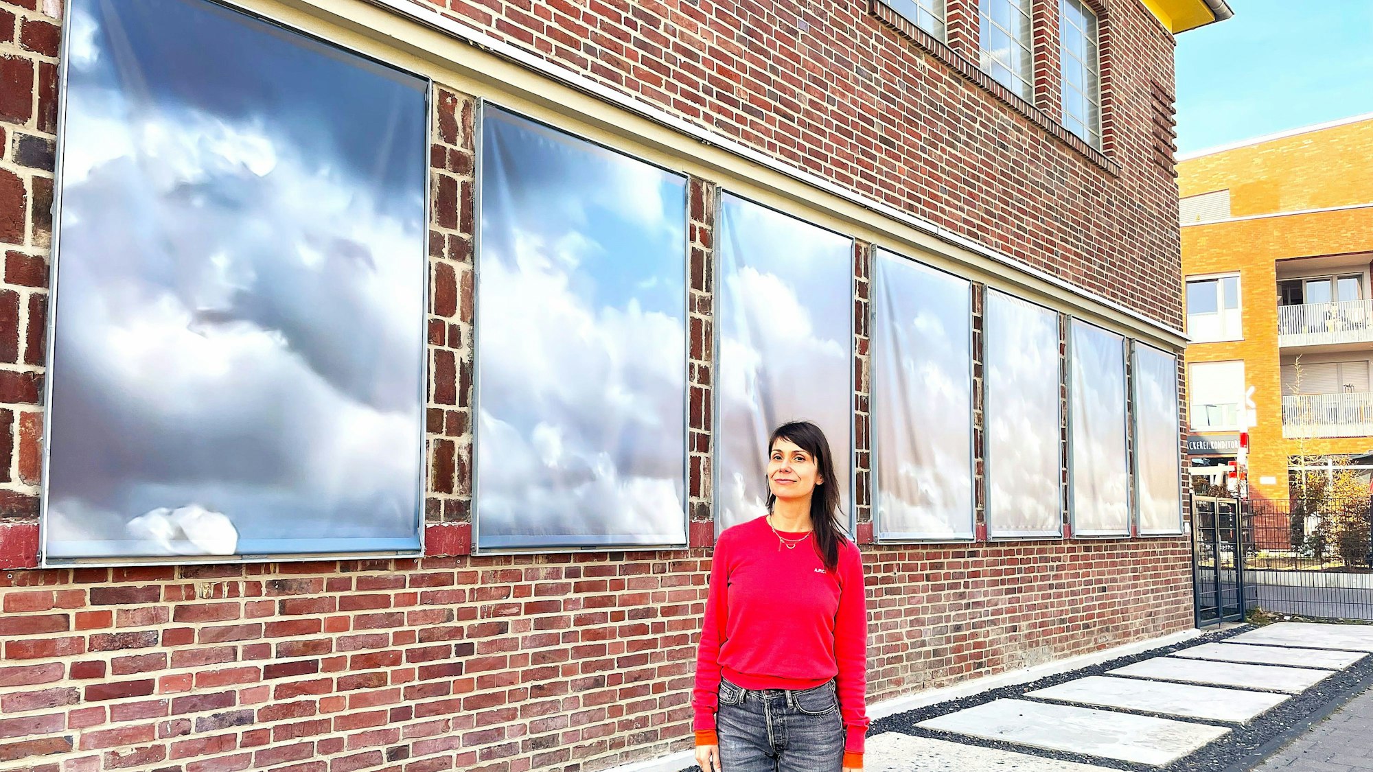 Die Zonta Preisträgerin Lyoudmila Milanova steht vor der Fuhrwerkswaage. An der Fassade hängen Wolkenbilder aus ihrem Video.