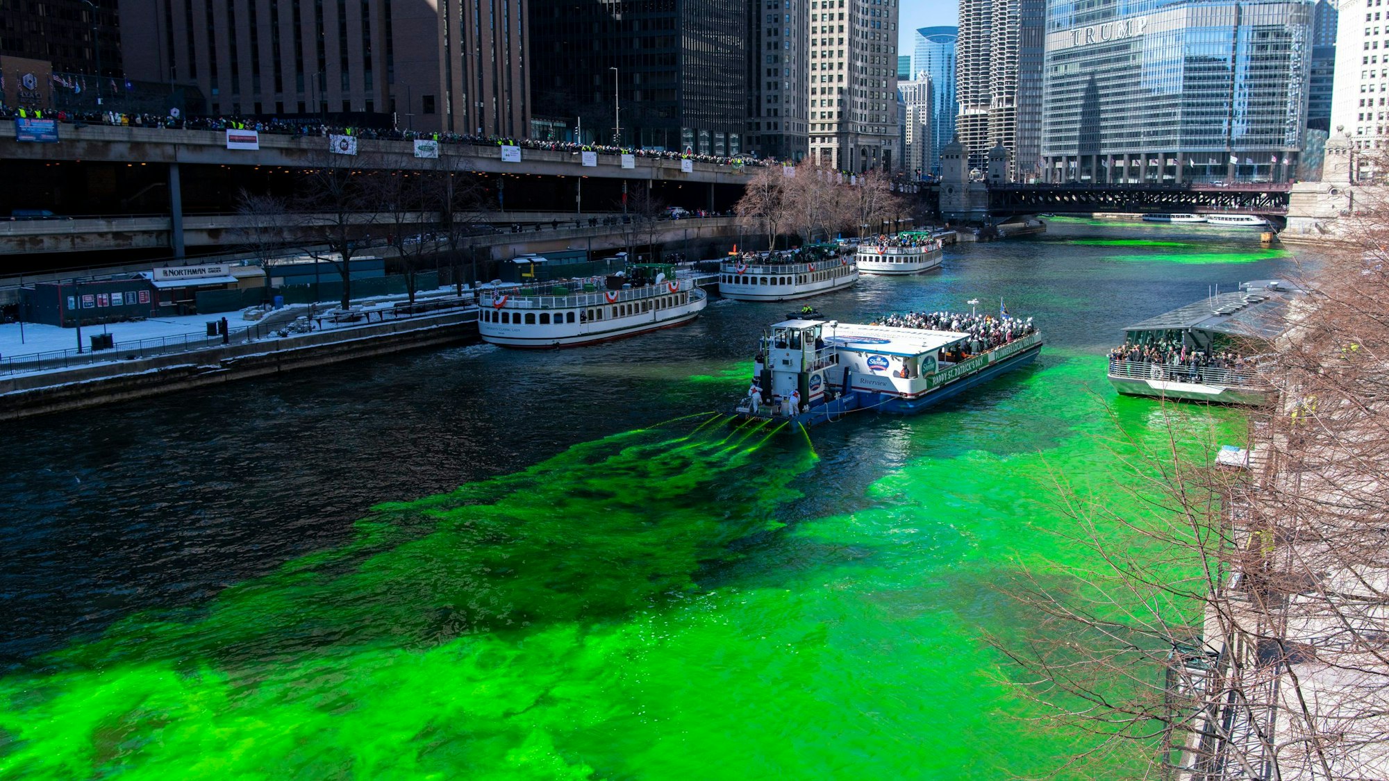 Aus einem Schiff kommt eine Flüssigkeit, die einen Fluss grün färbt. Im Hintergrund befinden sich Hochhäuser.