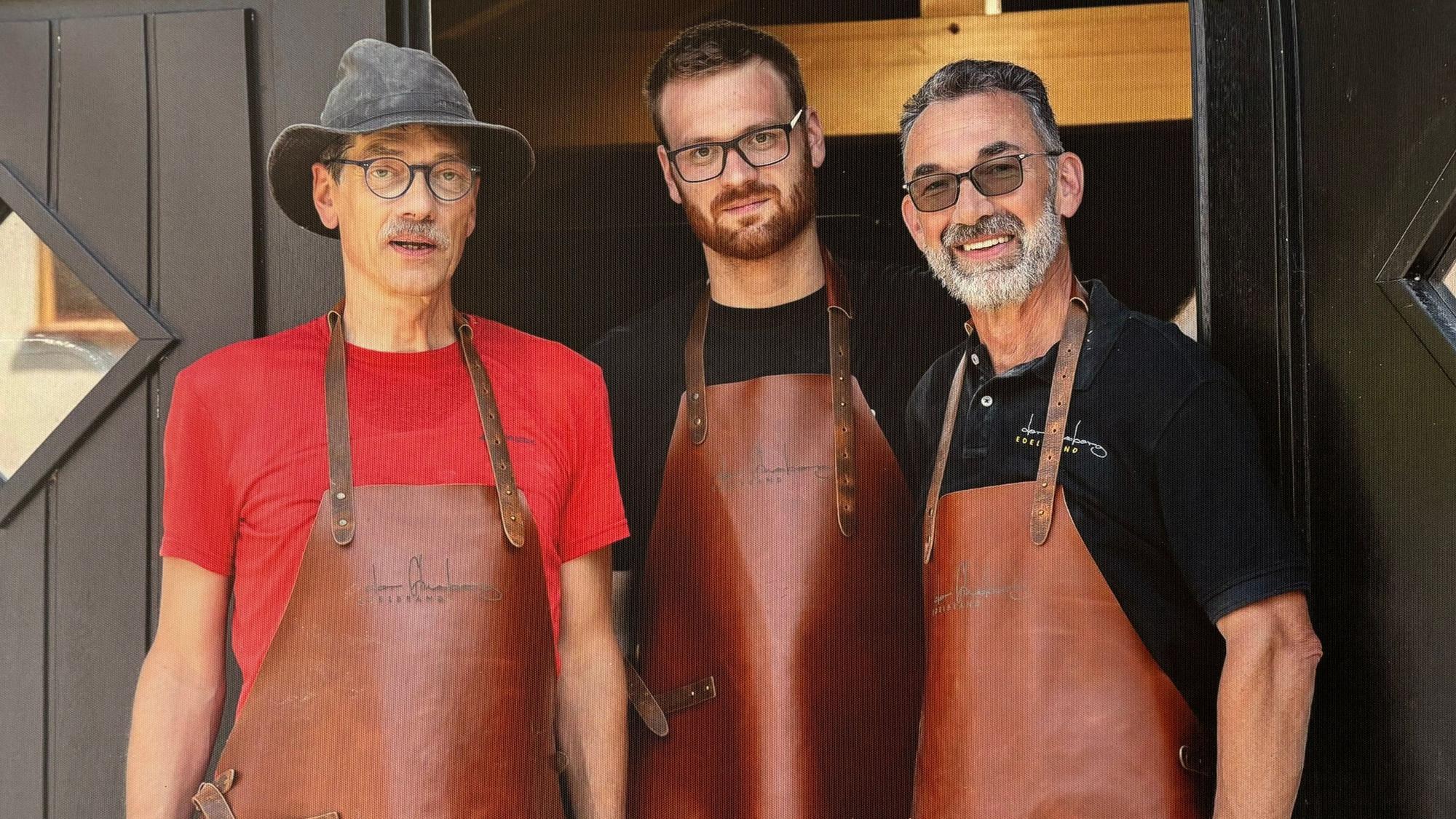 Drei Männer mit Lederschürzen schauen in die Kamera.