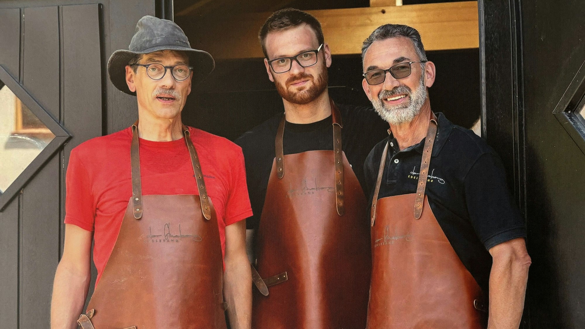Drei Männer mit Lederschürzen schauen in die Kamera.
