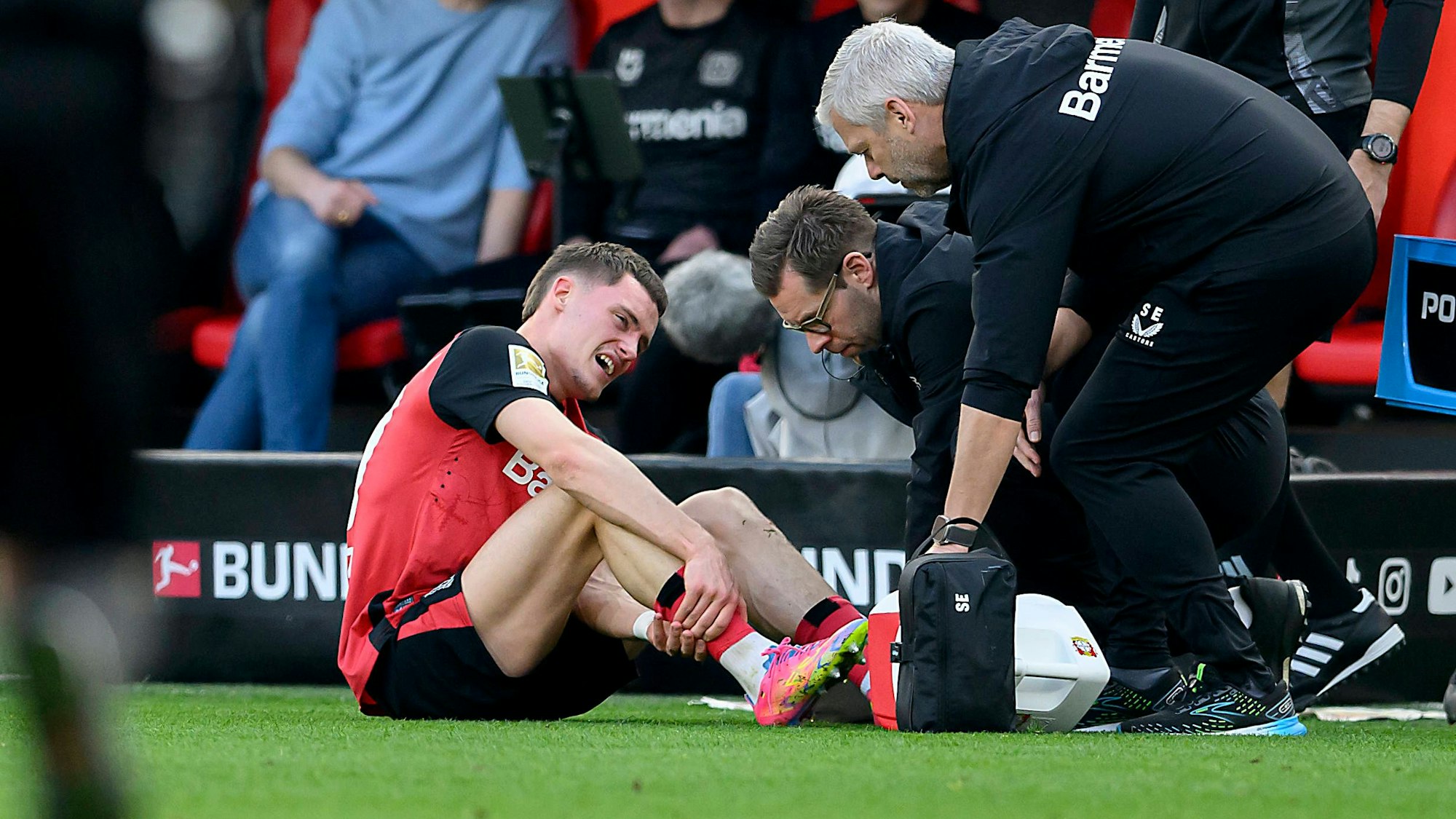 Florian Wirtz hält sich mit schmerzverzerrtem Gesicht das Bein, während er auf dem Rasen behandelt wird.