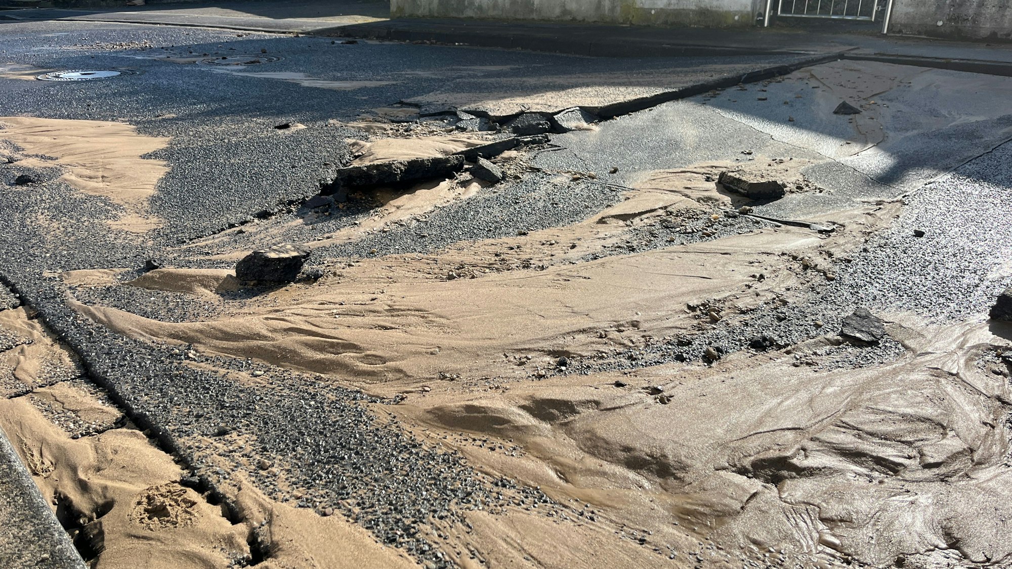Nach einem Wasserrohrbruch ist der Asphalt aufgebrochen, Schlamm ist auf der Straße verteilt.