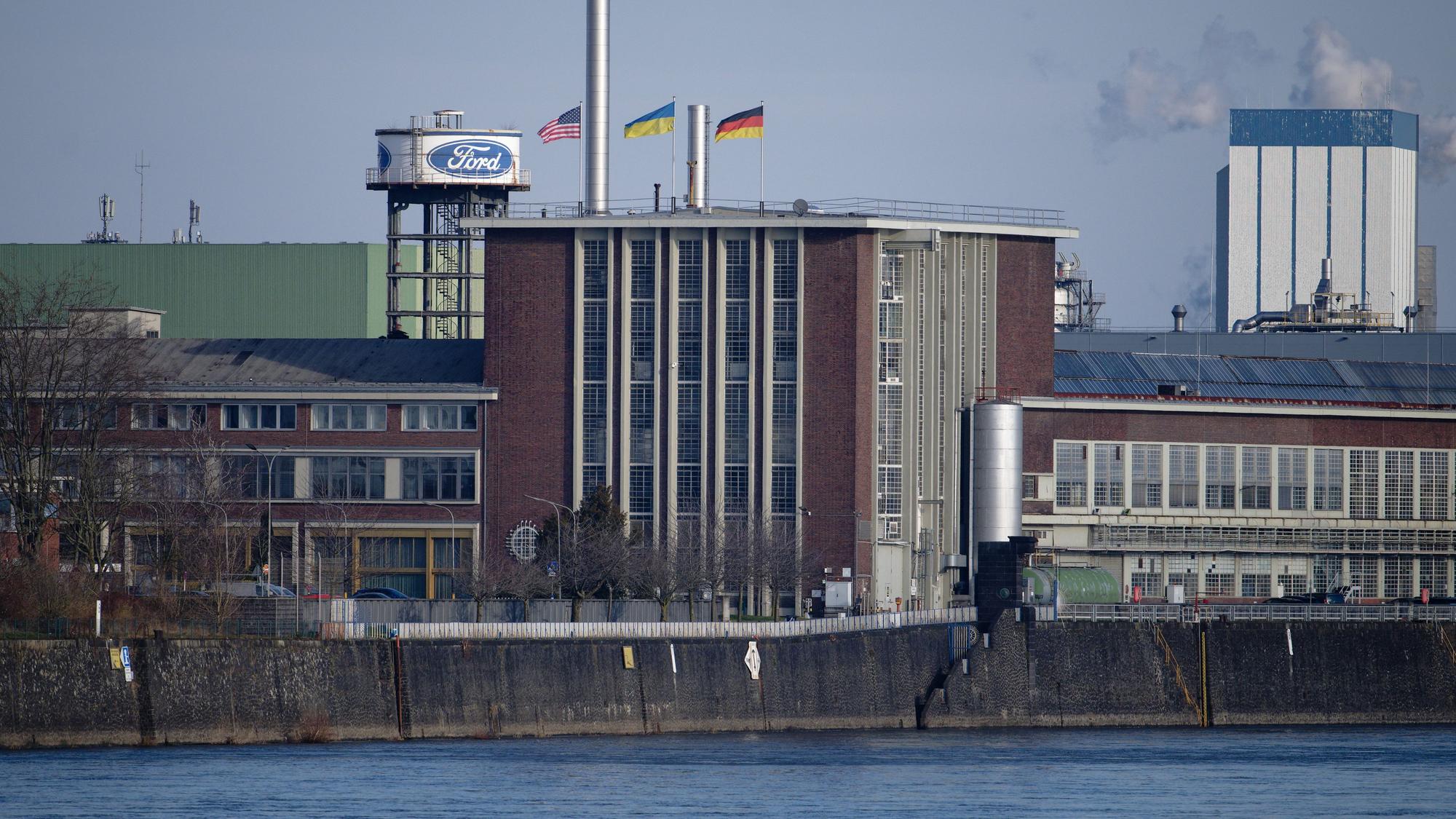 Die Flaggen der USA (l-r), der Ukraine und der Bundesrepublik Deutschland wehen über dem Dach eines Gebäudes der Fordwerke.