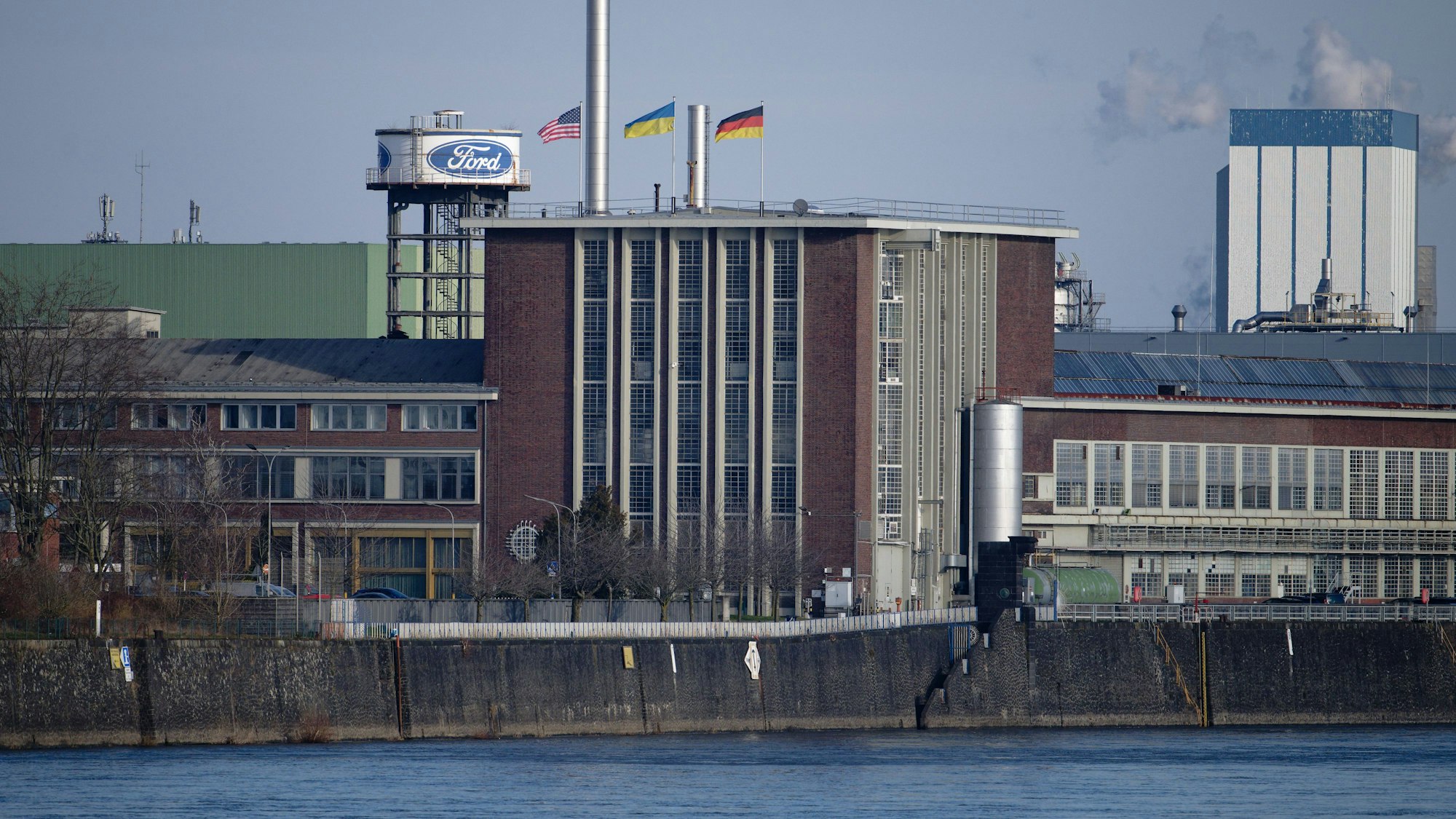 Die Flaggen der USA (l-r), der Ukraine und der Bundesrepublik Deutschland wehen über dem Dach eines Gebäudes der Fordwerke.