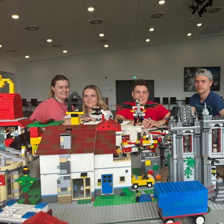 Vier junge Leute vor einer Lego-Stadt.