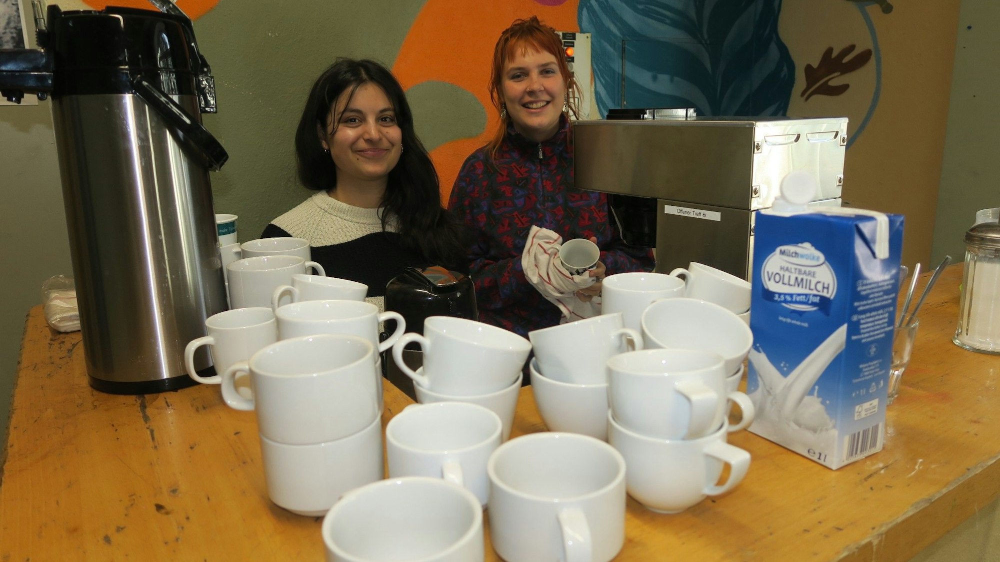 Zwei junge Frauen sitzen hinter einem Tisch mit Tassen.