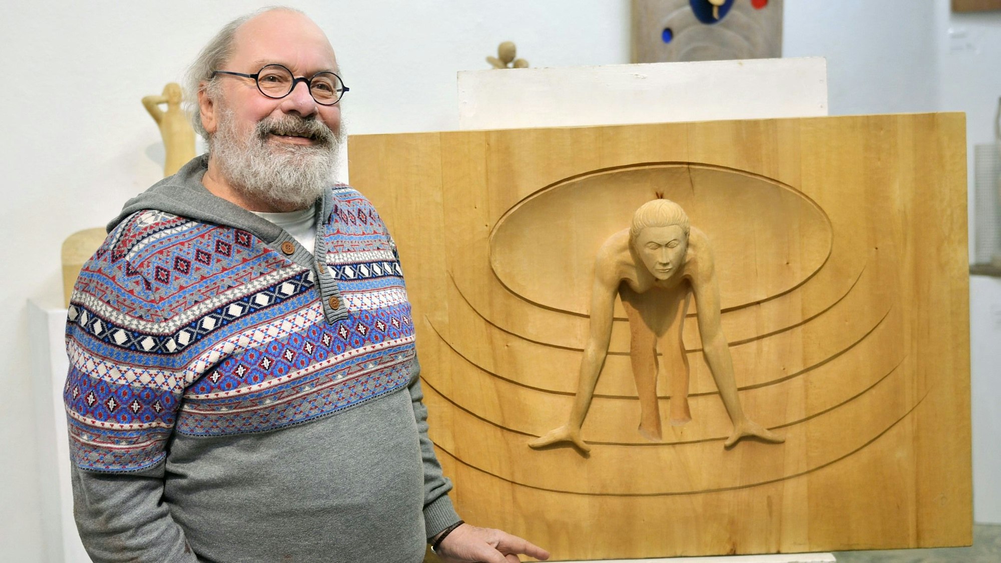 Der Bildhauer steht neben einem Relief, das eine Frau zeigt, die in den Startlöchern zu stehen scheint.