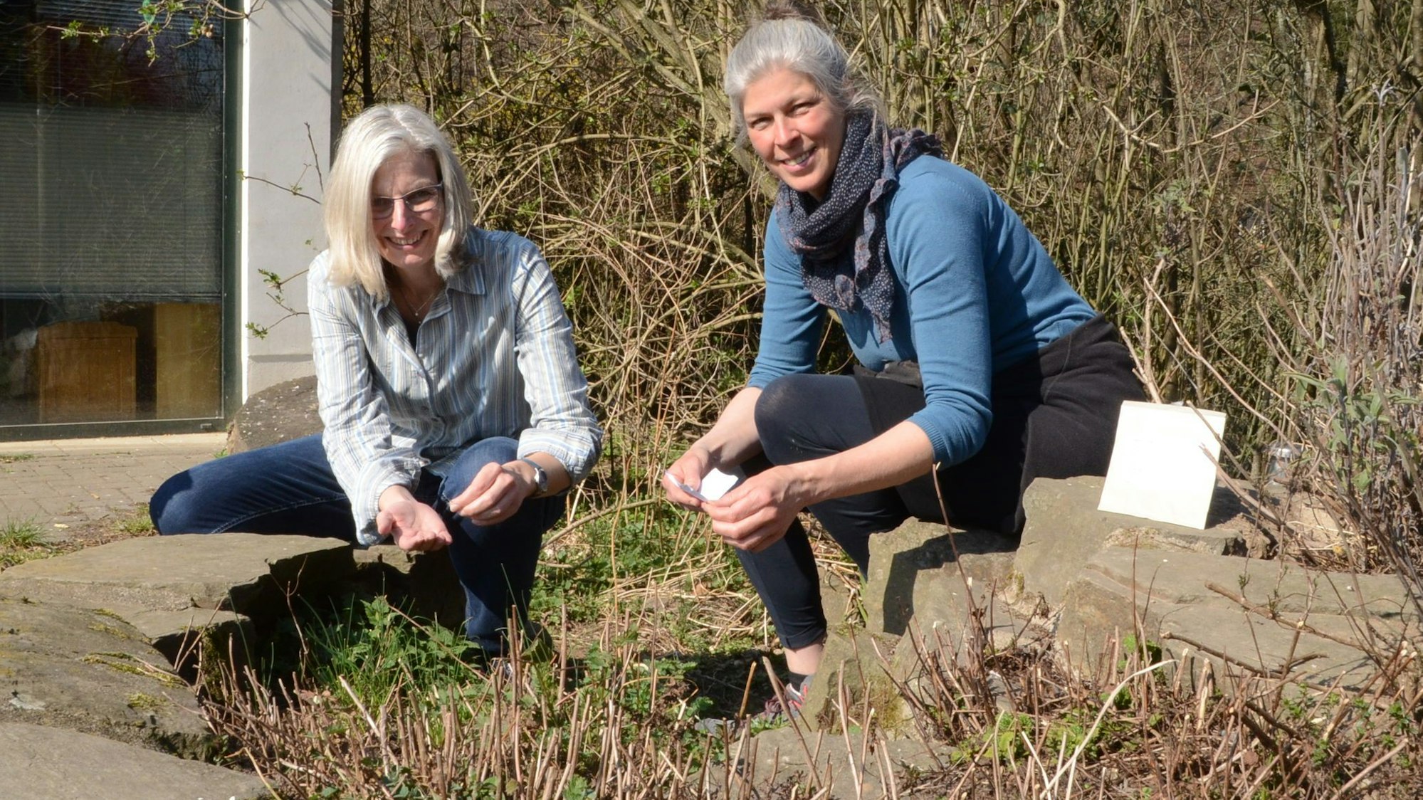 Zwei Frauen sitzen in der Hocke in einem Garten.