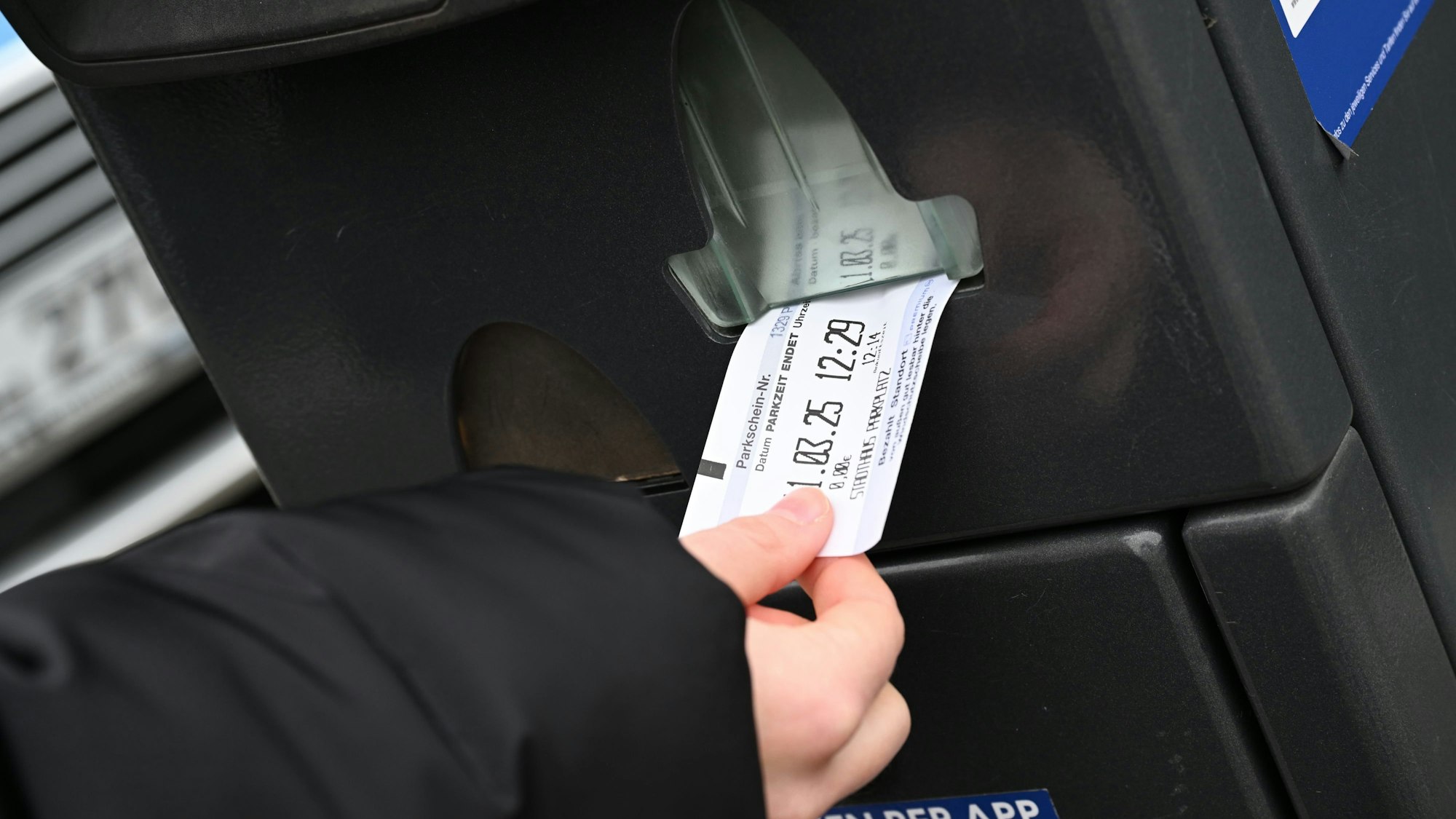Eine Hand zieht einen Parkschein aus einem Automaten.