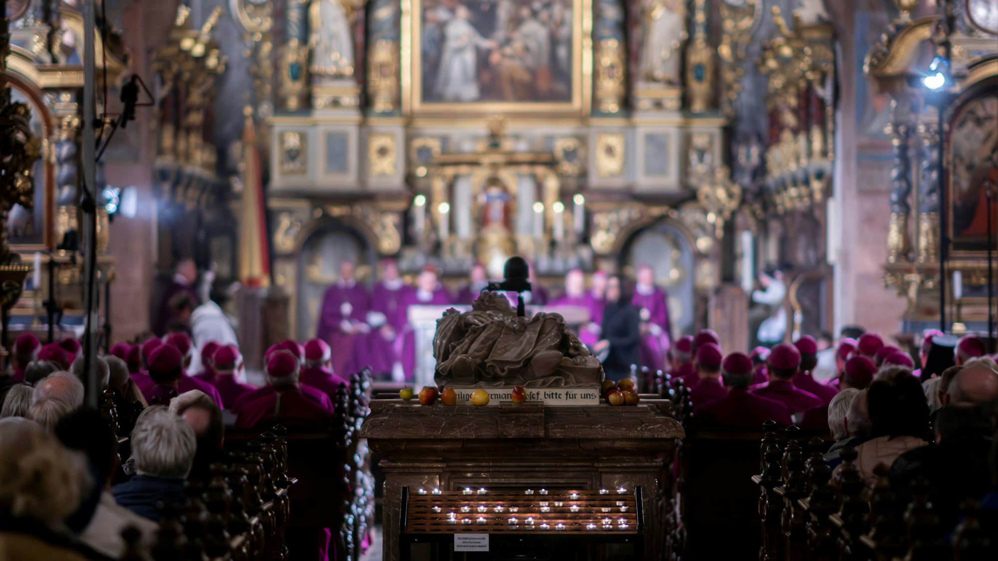 Der Sarkophag des heiligen Hermann-Josef ist im Mittelgang der Steinfelder Basilika zu sehen. Rechts und links sitzen Gläubige in den Bänken, im Hintergrund sind zahlreiche Priester am Altar.