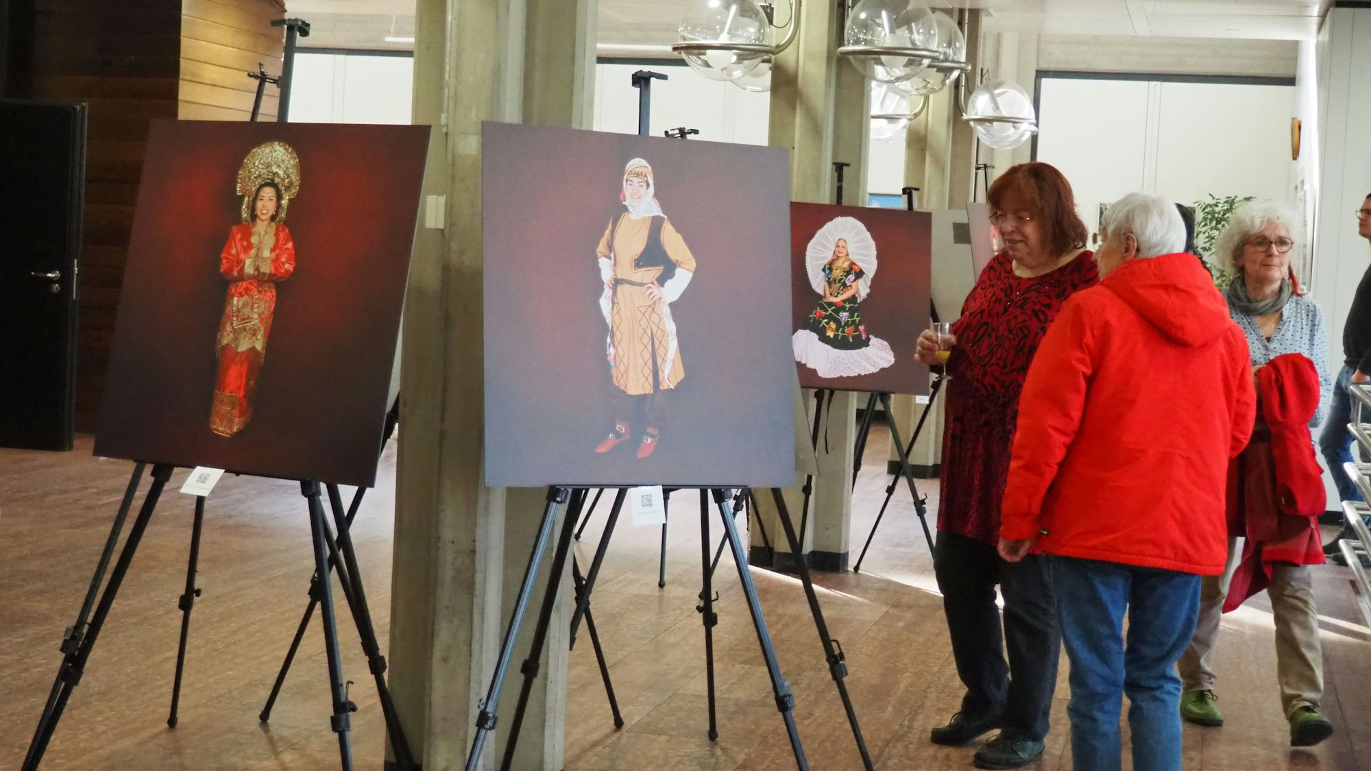 Auf Staffeleien stehen Fotos von Frauen, Besucherinnen betrachten die Bilder-