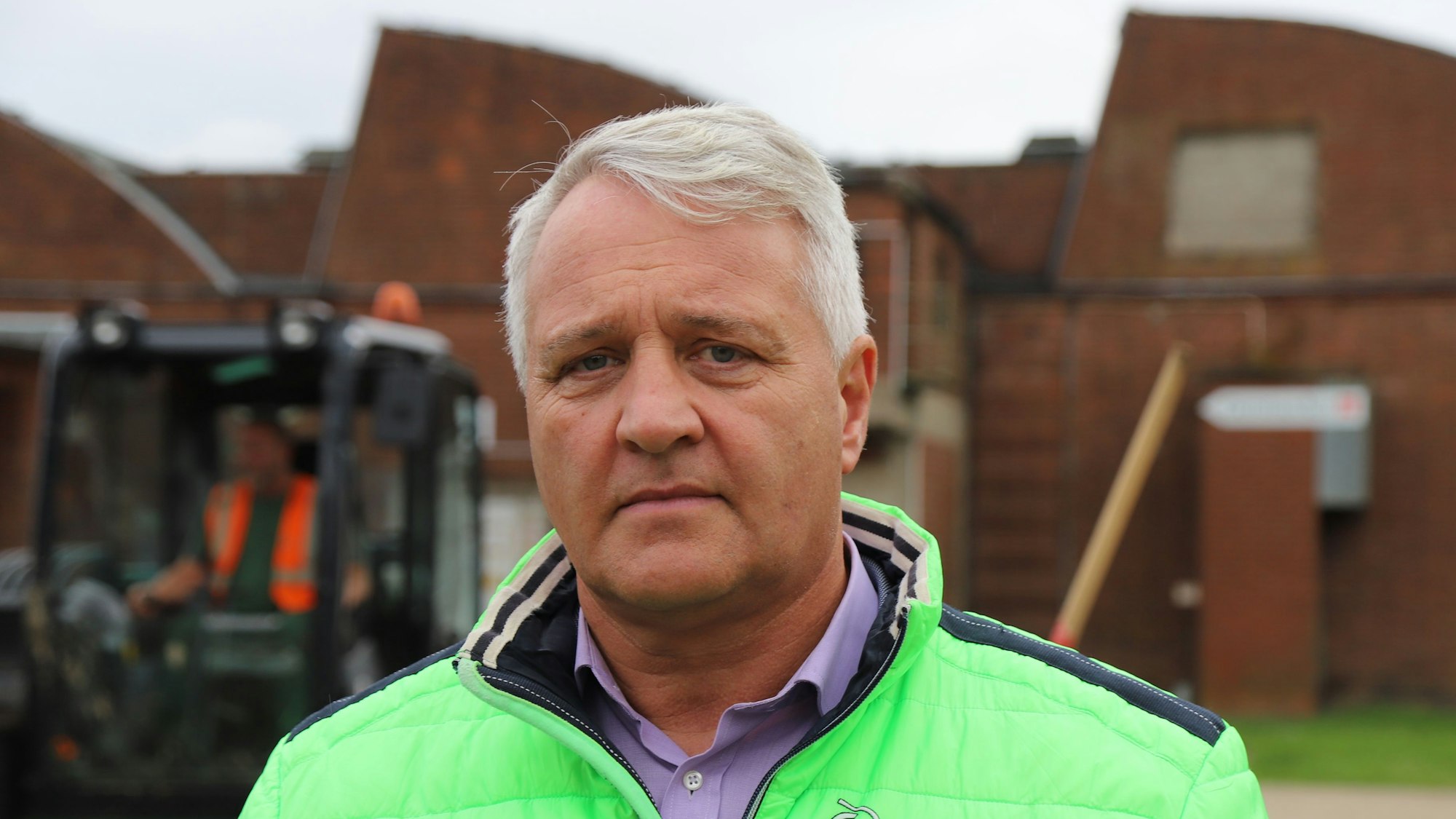 Ein Mann in einer neongrünen Winterjacke steht vor einer alten Industriehalle.