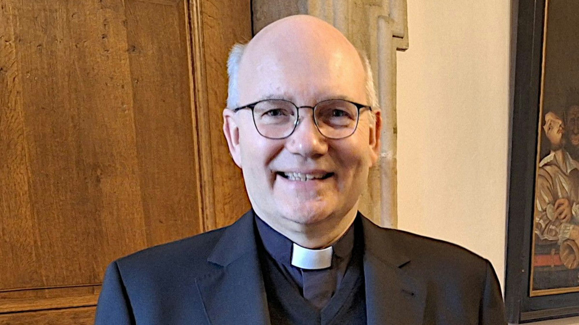 Ein Mann in dunklem Anzug steht vor einer Holztür.