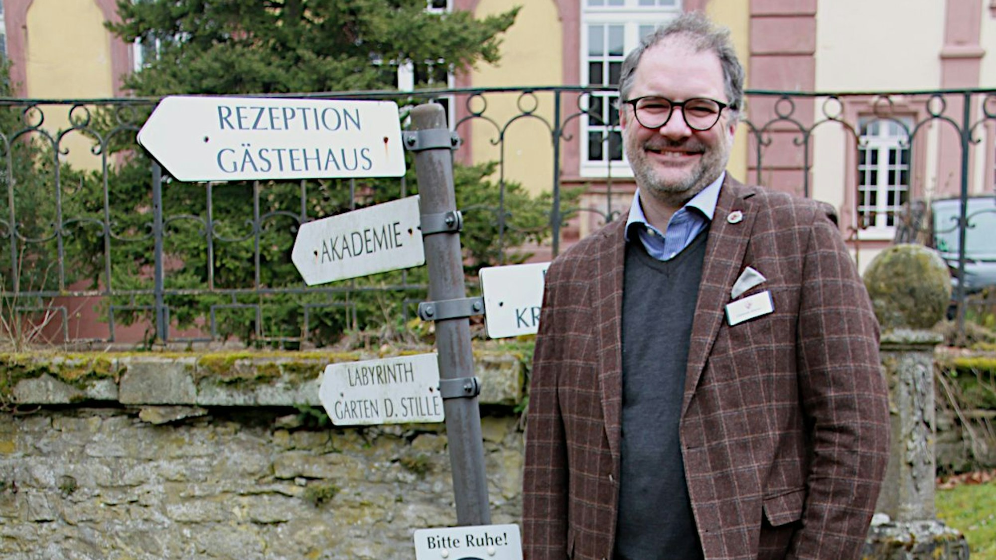 Ein Mann in kariertem Sakko steht auf einer Wiese.