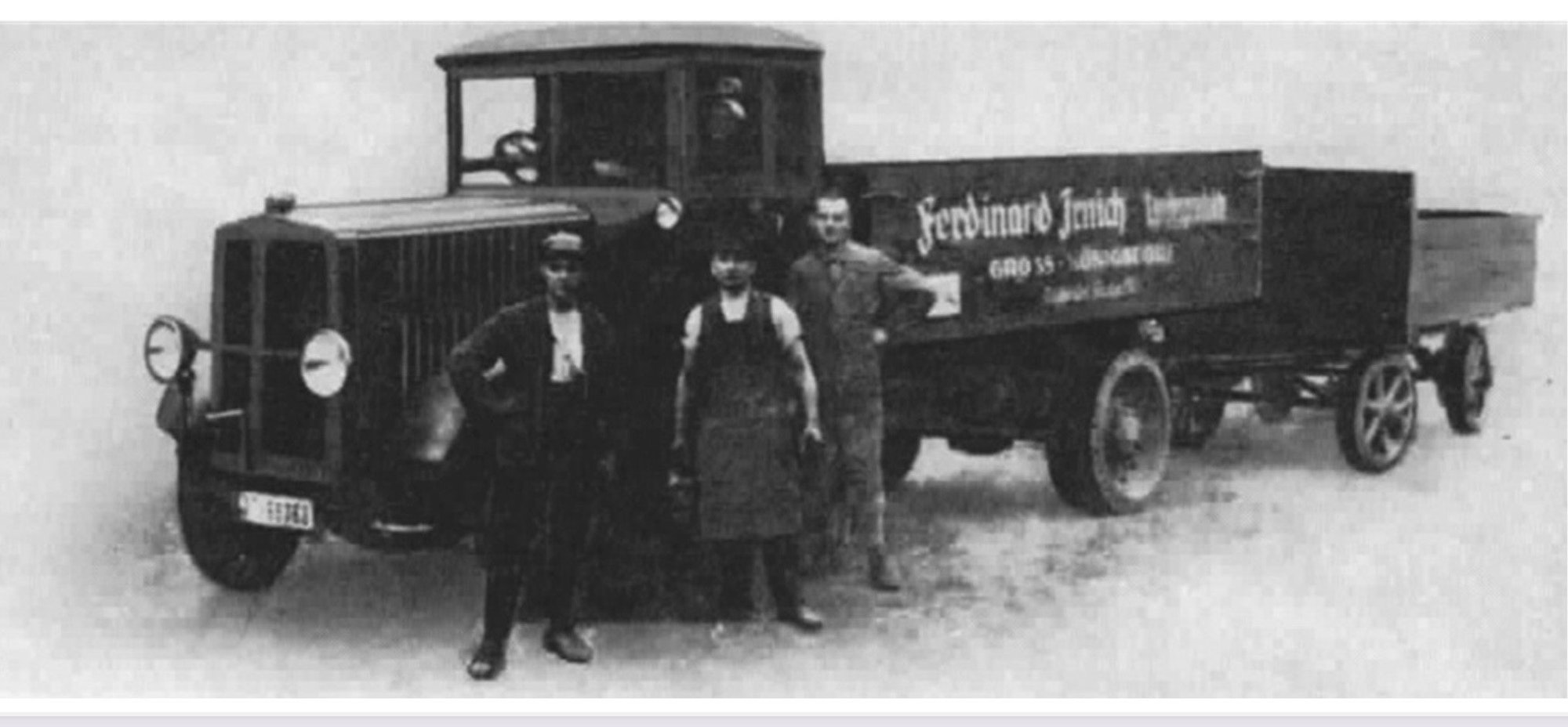 Auf dem Bild ist eine SW-Aufnahme eines historischen Lkws zu sehen, vor dem drei Männer stehen.