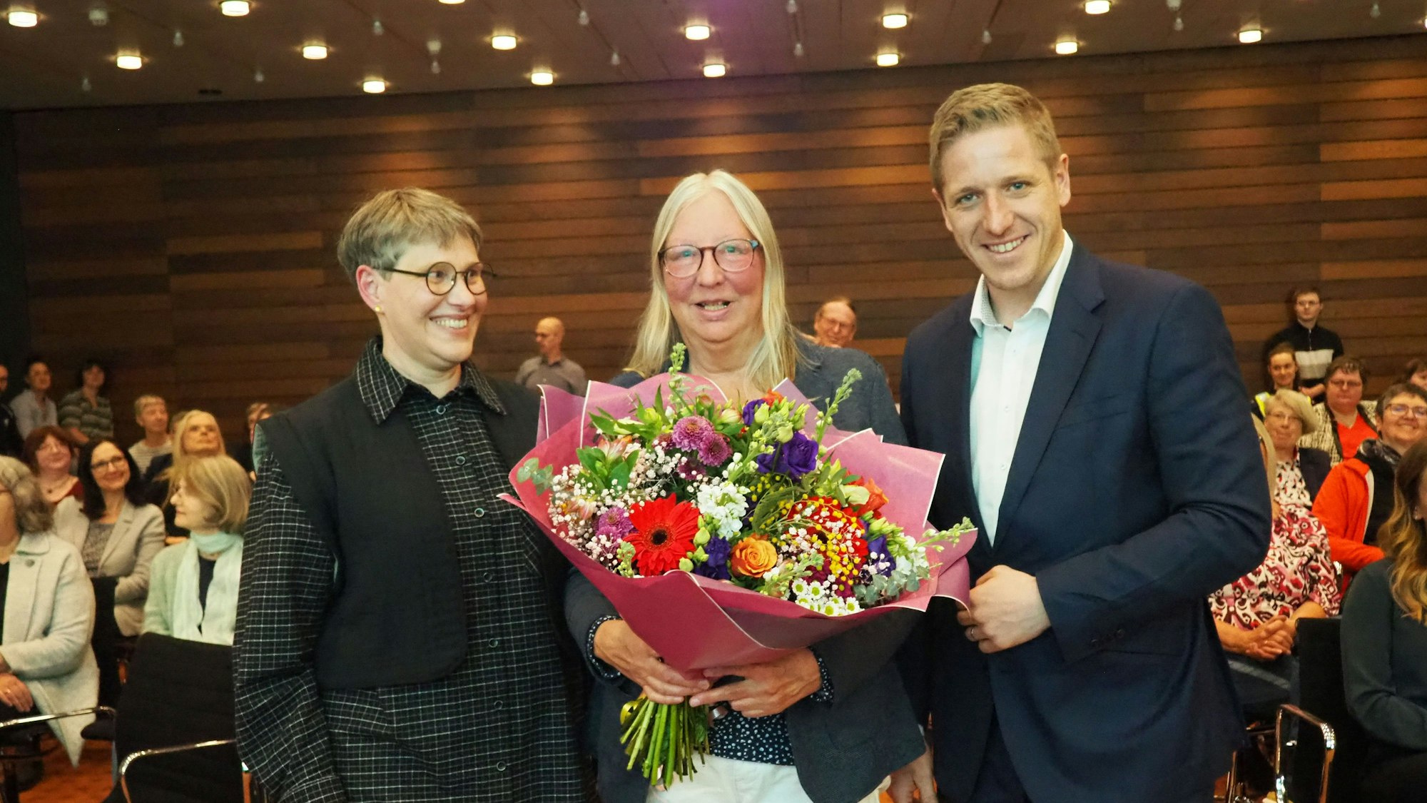 Astrid Günther, Ellen Mende und Markus Ramers stehen nebeneinander. Mende hält einen Blumenstrauß.